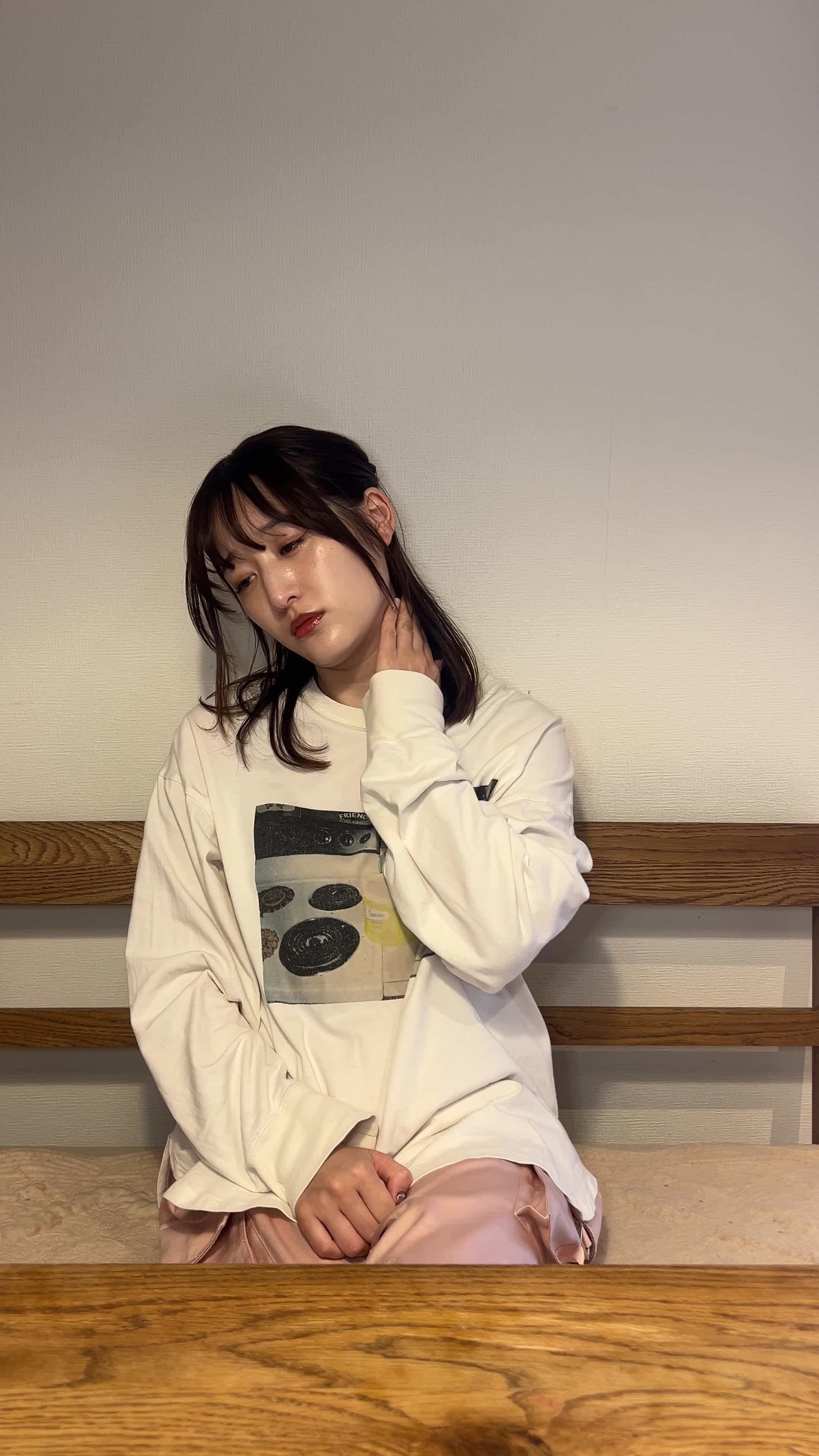 壁にもたれながら、手で軽く首元を押さえて肌を気にしている表情を見せる