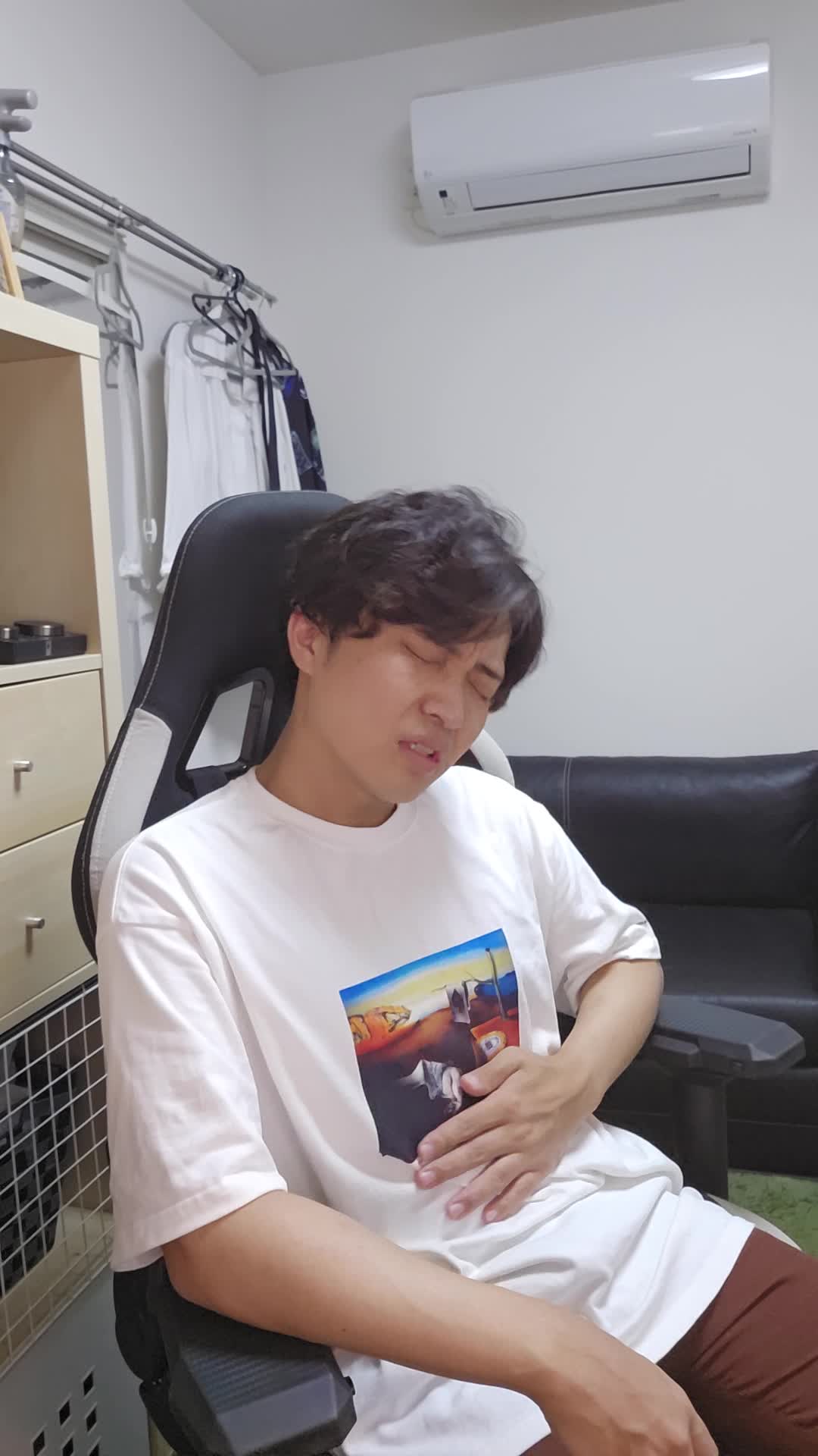 椅子に座り、お腹を軽く押さえながら「ずっと痛みが続いている…」と苦しそうな表情