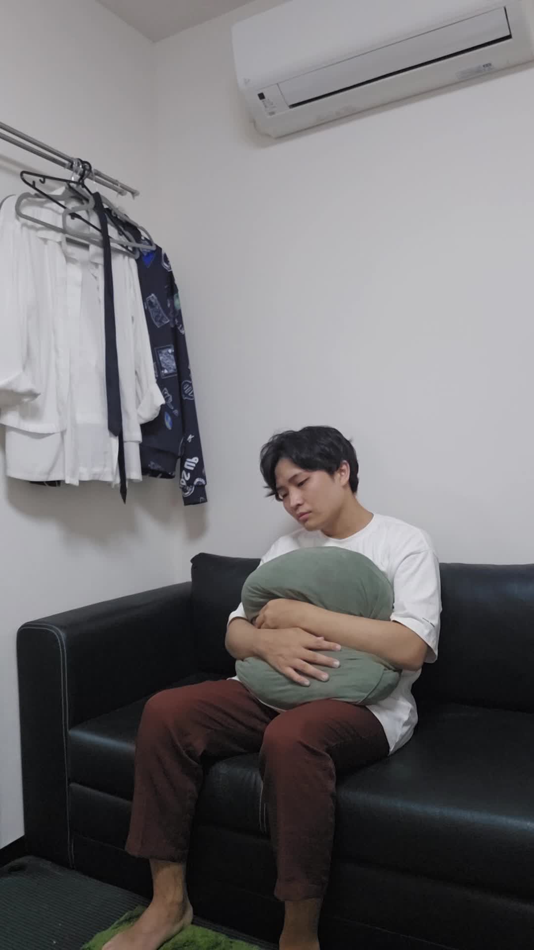 ソファでクッションを抱え、「腸が動いていない感じがして不安そうに考える」表情