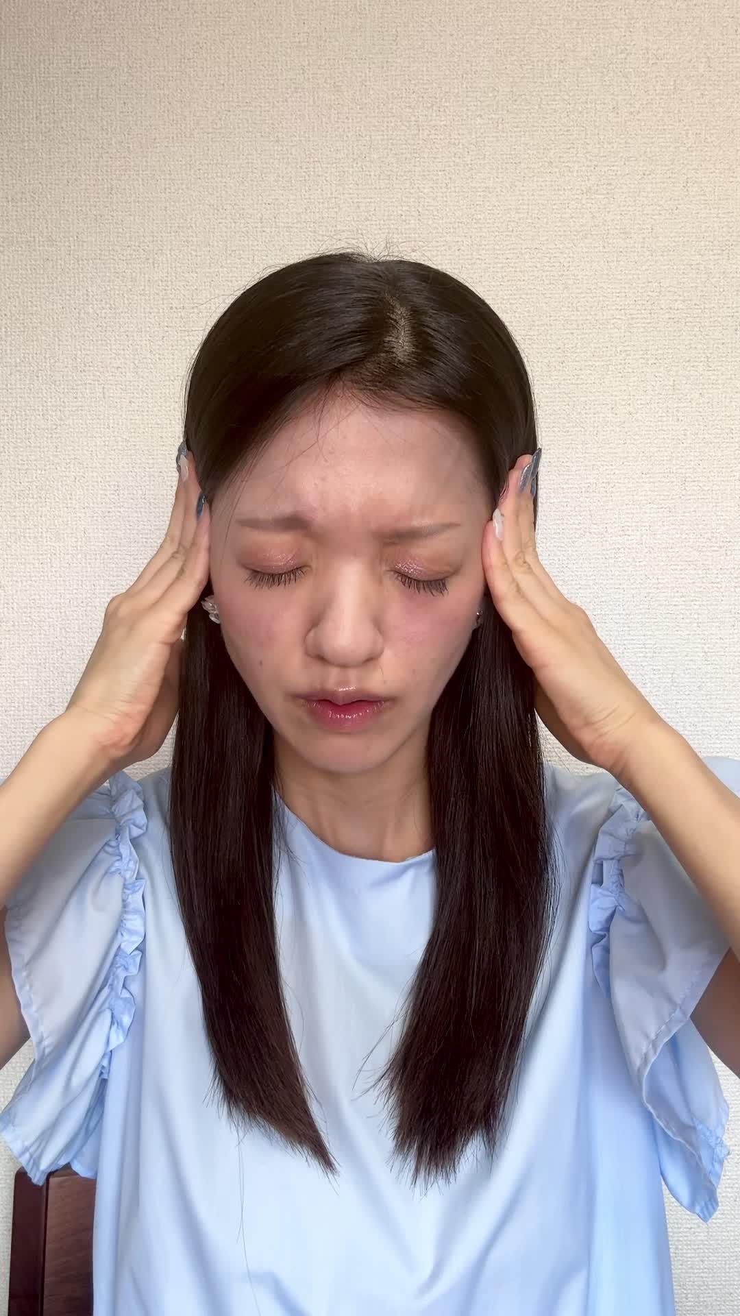 椅子に座り、手でこめかみを押さえながら「最近ずっと頭が重い」と困った表情