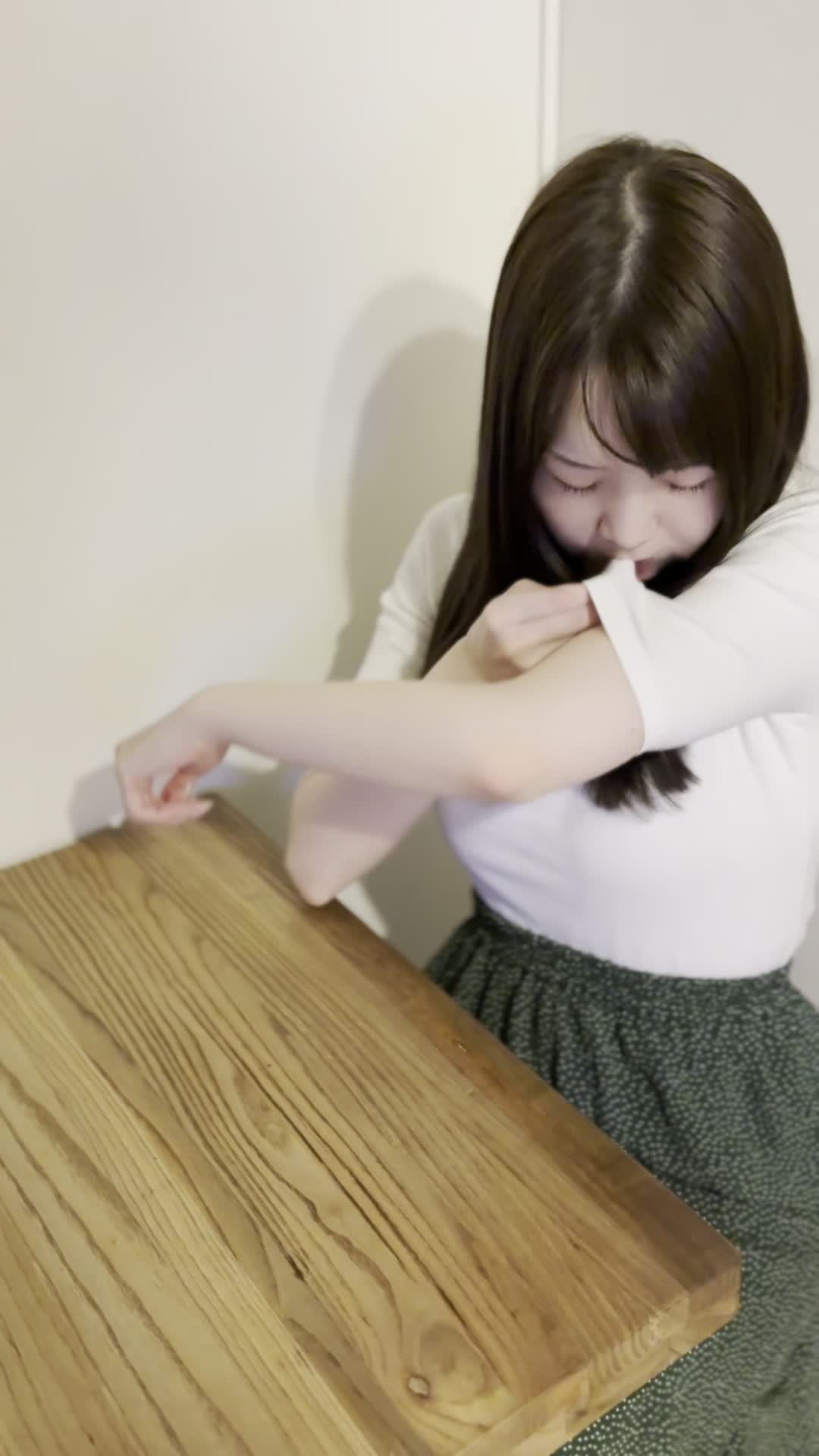 椅子に座り、少し緊張した表情で自分の服の袖を軽く嗅ぐ様子