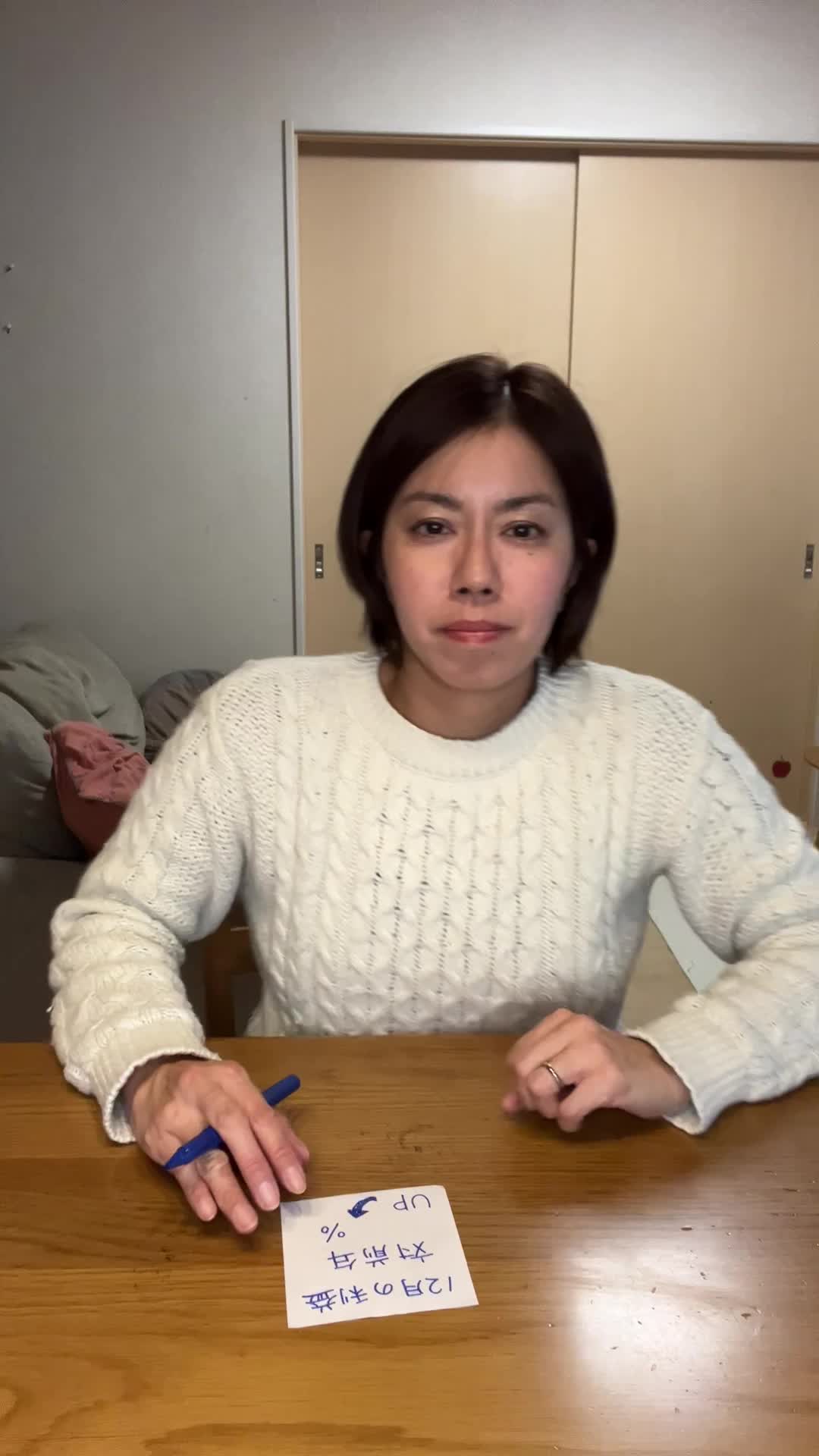 テーブルで数字を書き込んだメモを画面に向けて提示し、「これが成果だ」と見せる動き