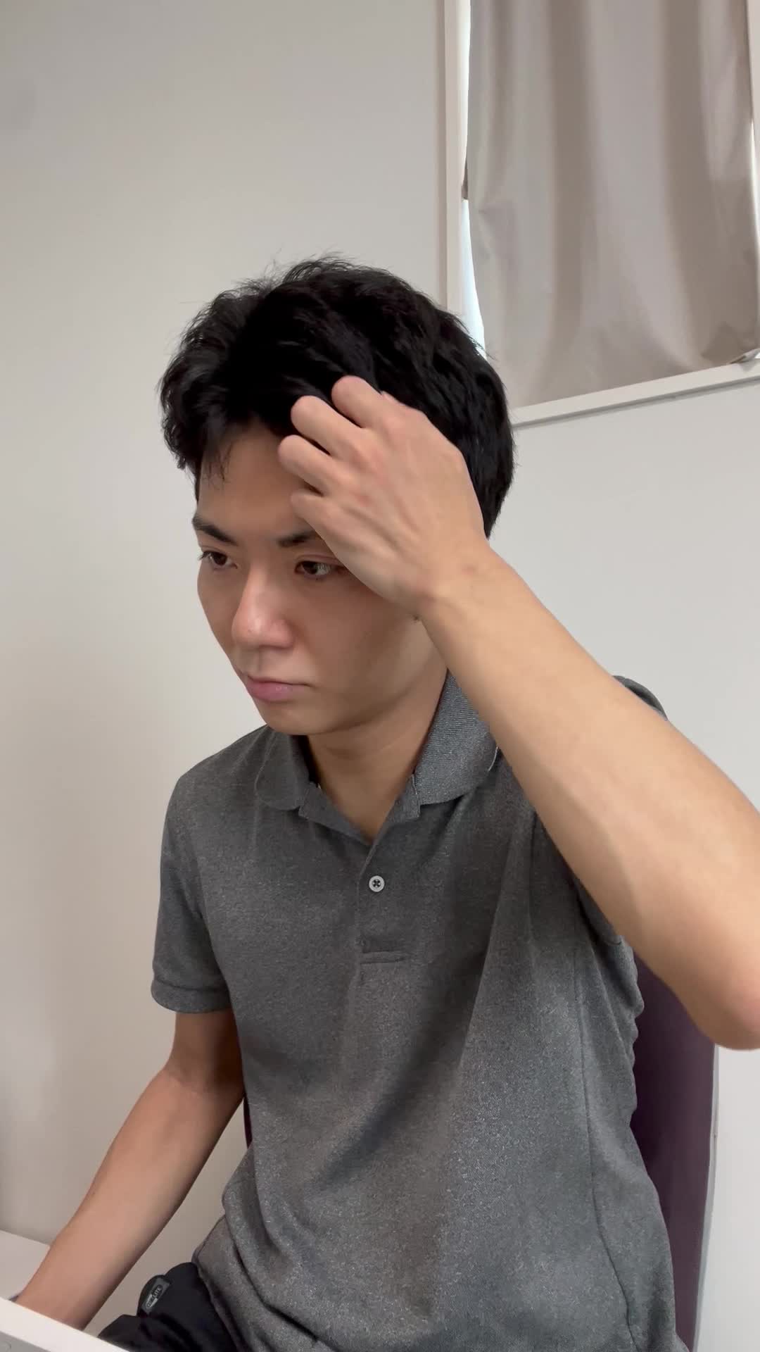 椅子に浅く腰掛け、髪を手ぐしで整えながら「このシャンプー試してみよう」と決意する表情