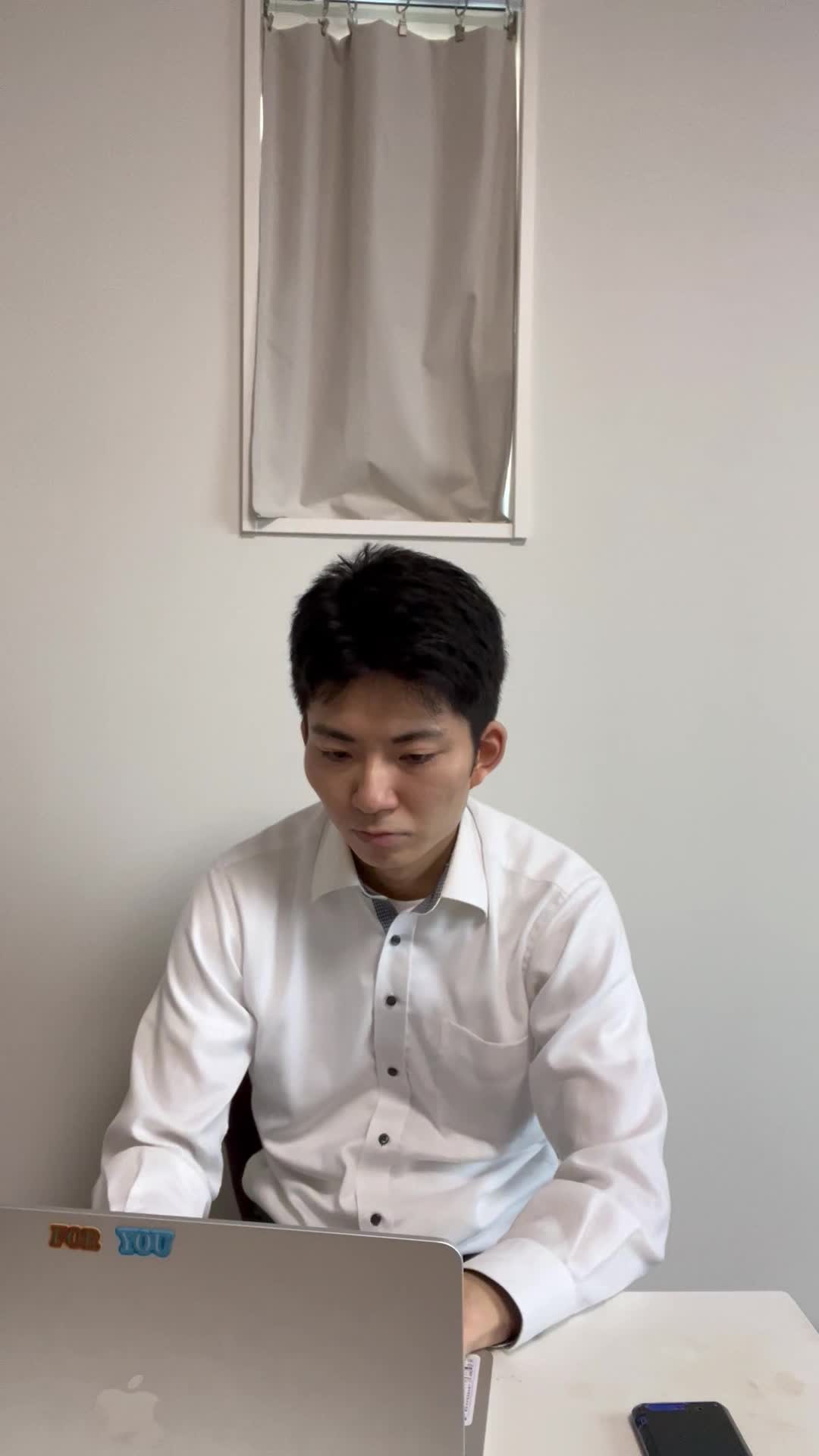 椅子に座り、仕事中にスマホを確認し、メッセージが来てにやけてしまう様子