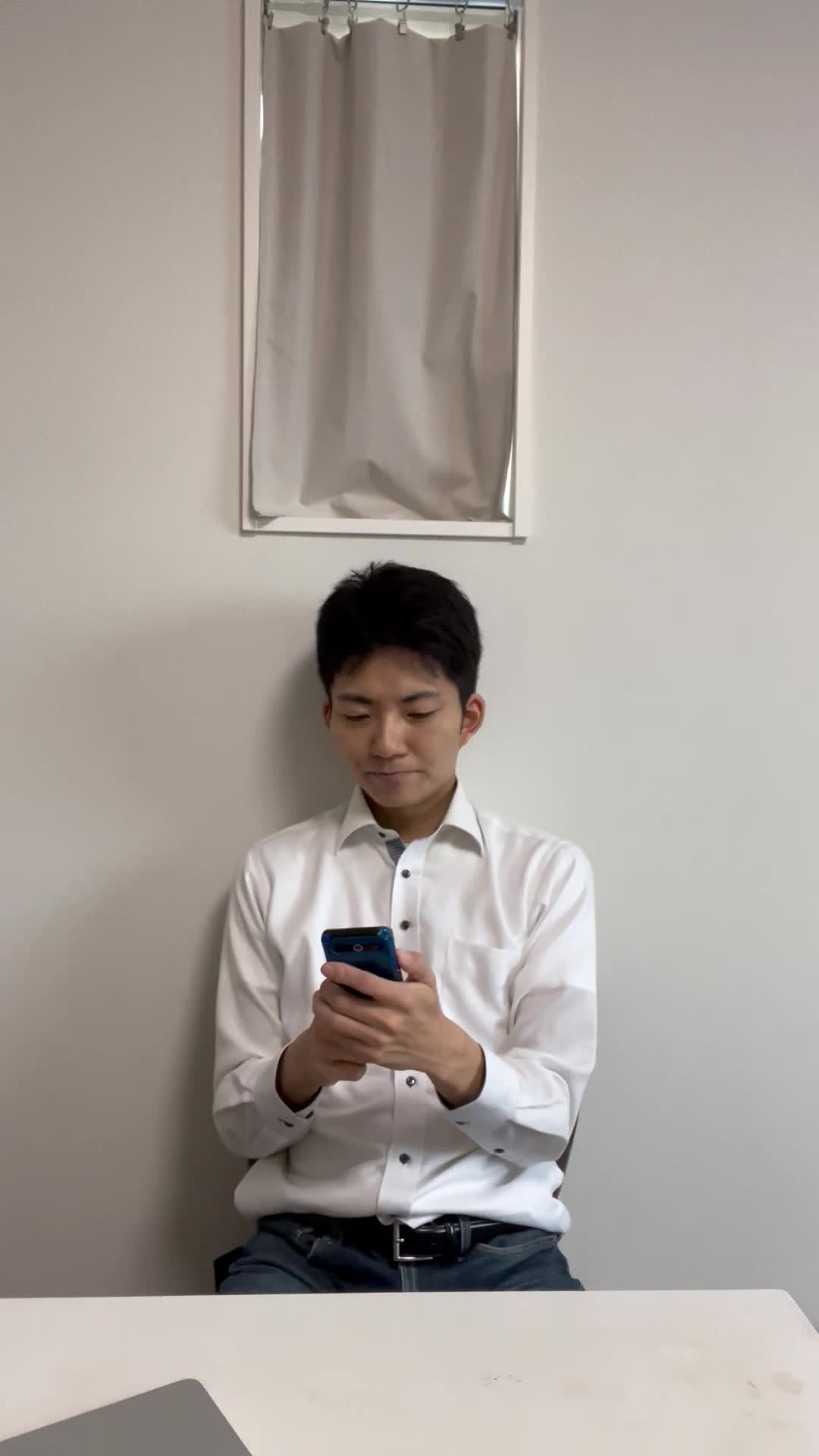 椅子に腰掛け、スマホのメッセージをじっと見つめて微笑むシーン