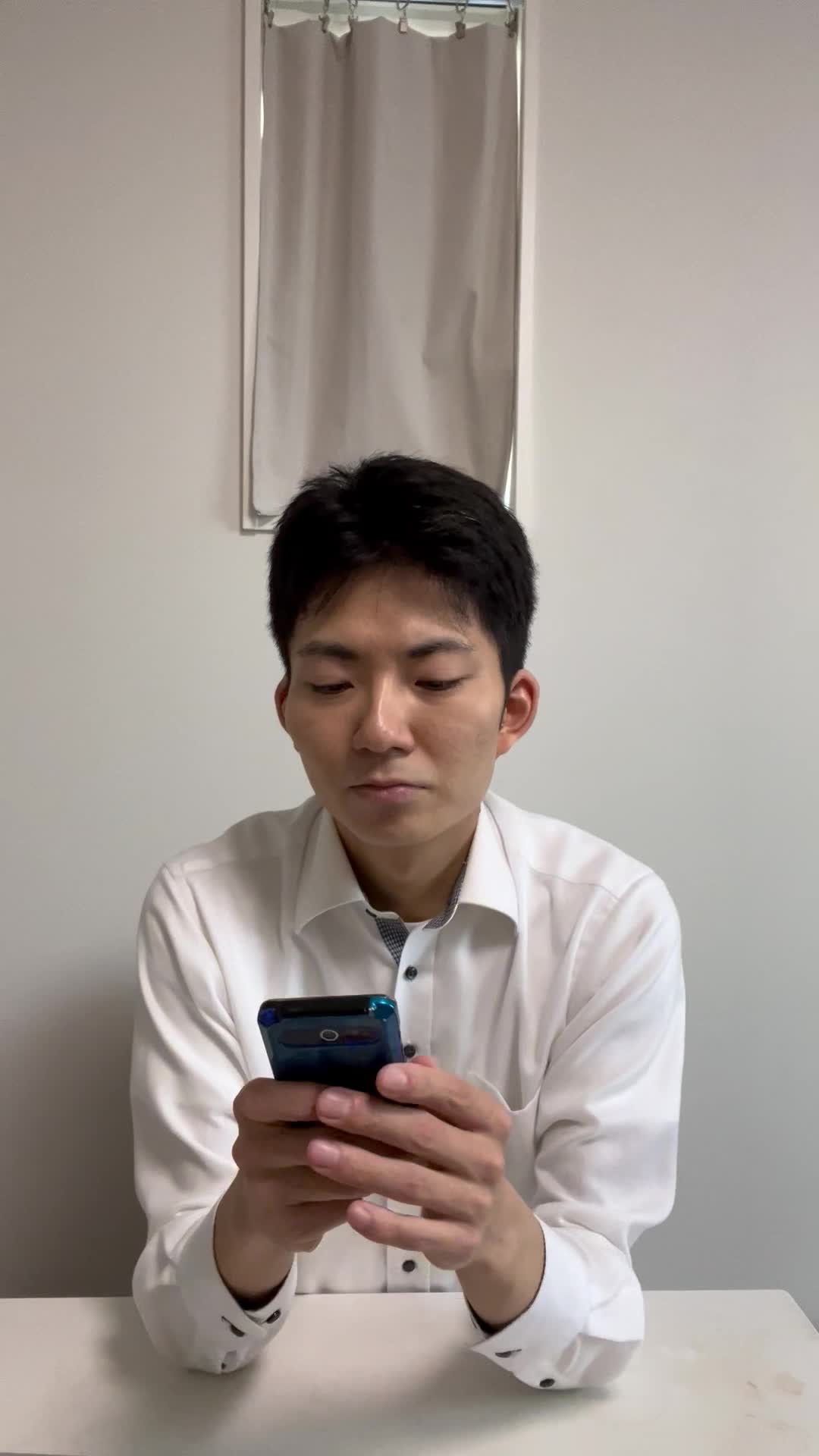 椅子に浅く腰掛け、スマホを握りしめながら「次のメッセージ、早く来ないかな」と待つ動作