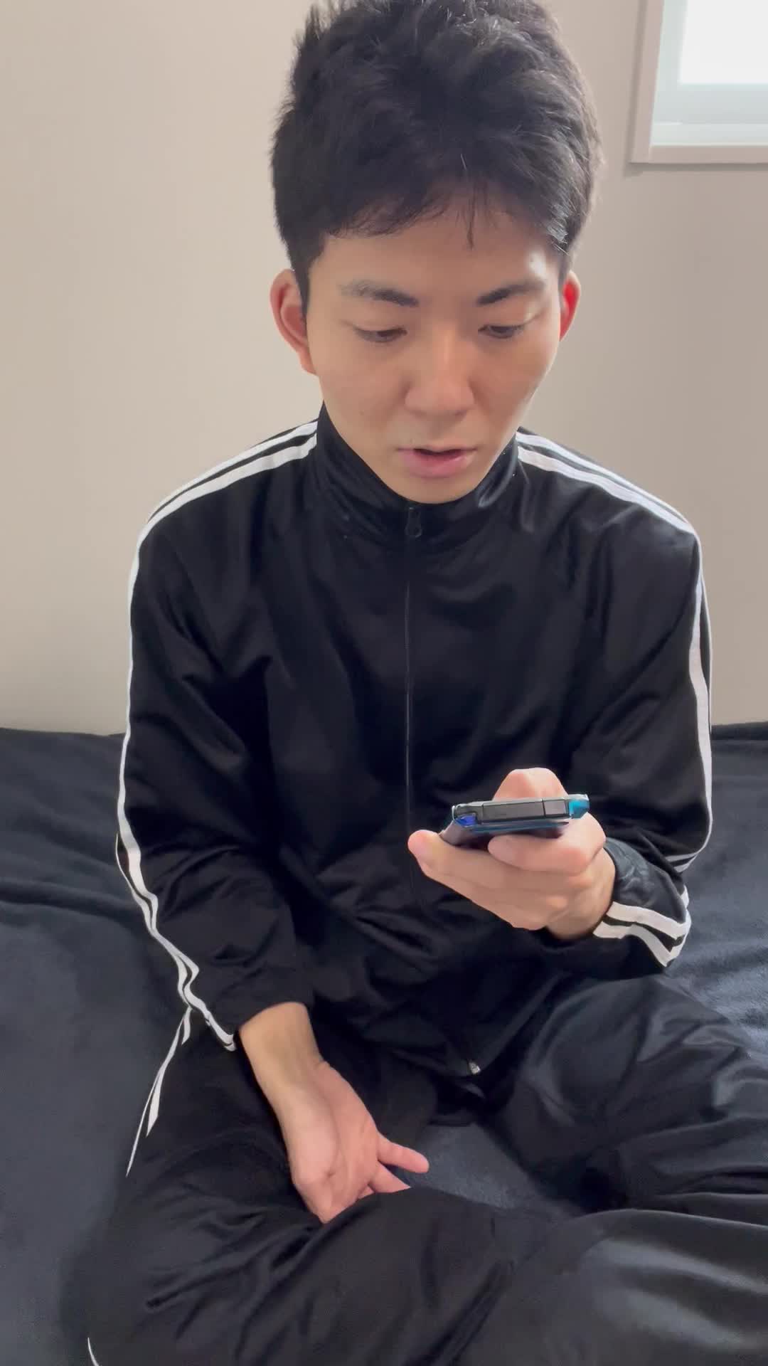 ベッドに座り、スマホを見つめながら軽くため息をつき、また微笑む様子