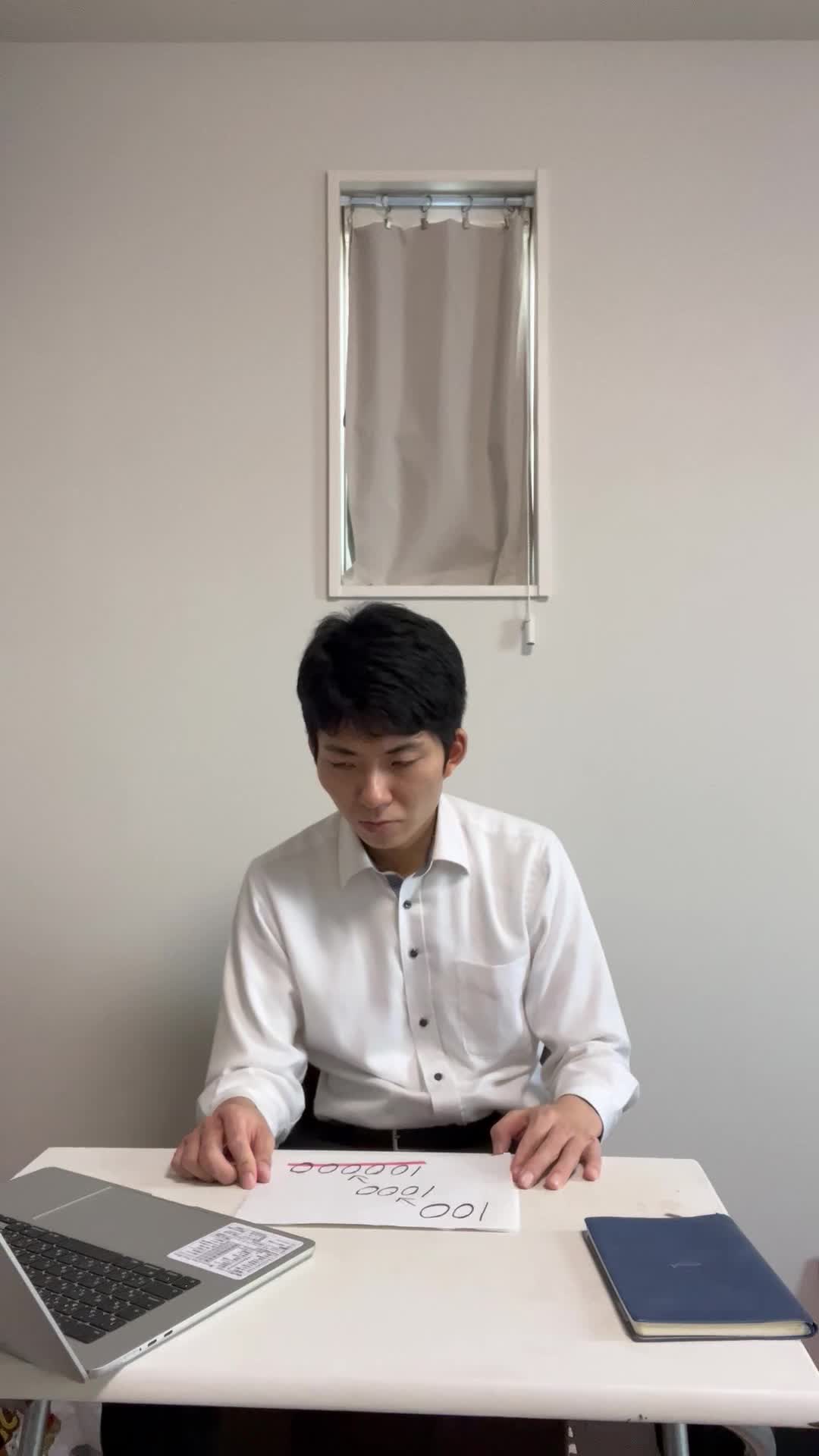 テーブルで紙をめくり、数字を指差しながら「これか！」と閃いた表情を浮かべる姿