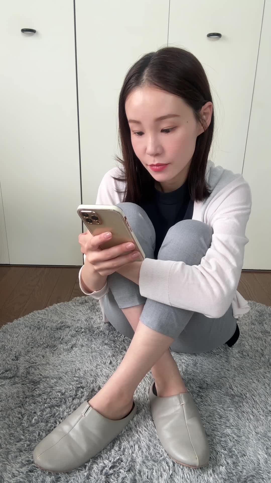 床に座り込み、スマホで「保険の口コミ」を見ながら少し安心した表情を浮かべる