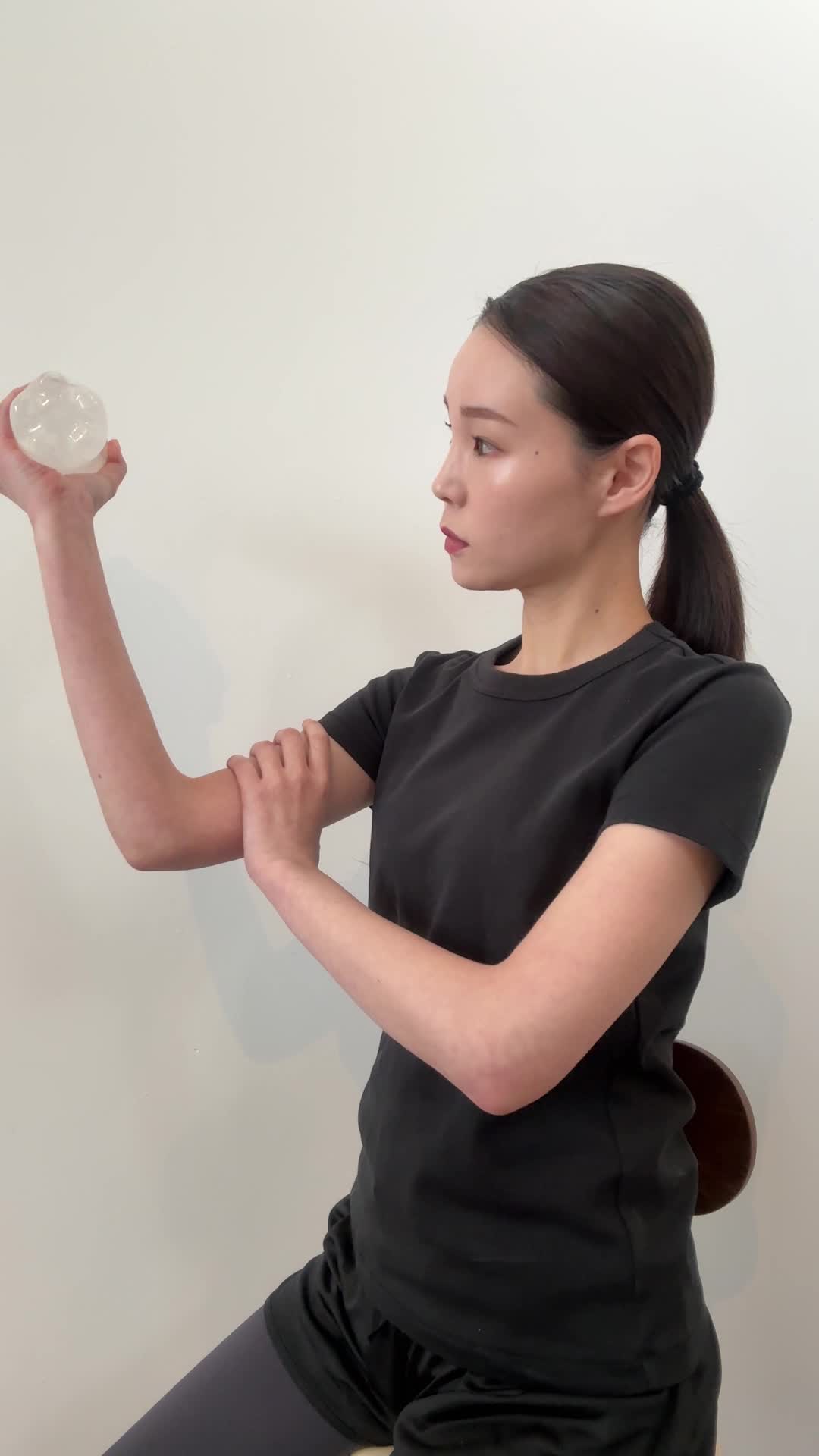 椅子に座り、ペットボトルをダンベル代わりにして軽く腕を曲げる仕草