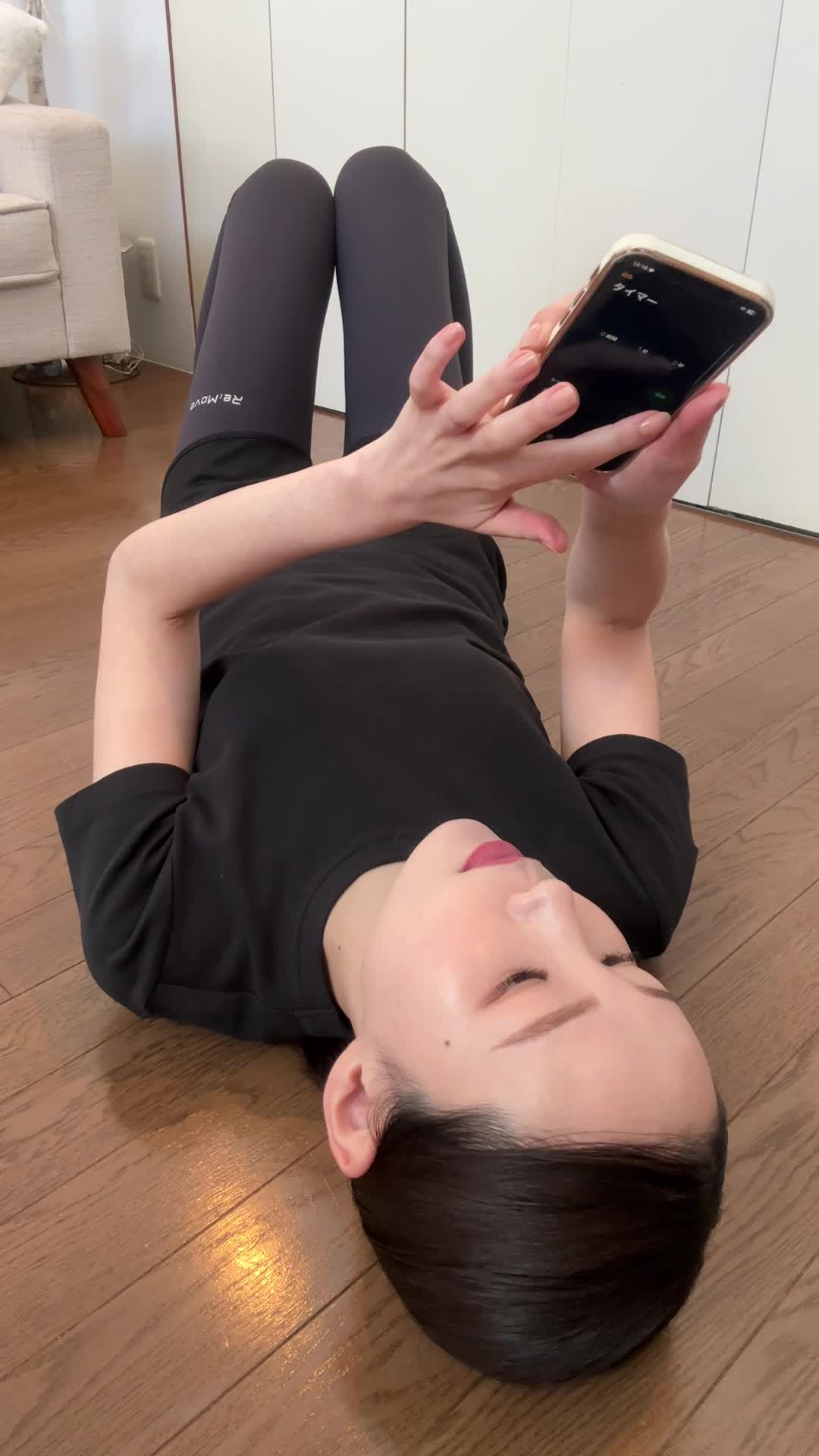 床に寝転び、仰向けになって「1分間プランク」のタイマーをセットする動作