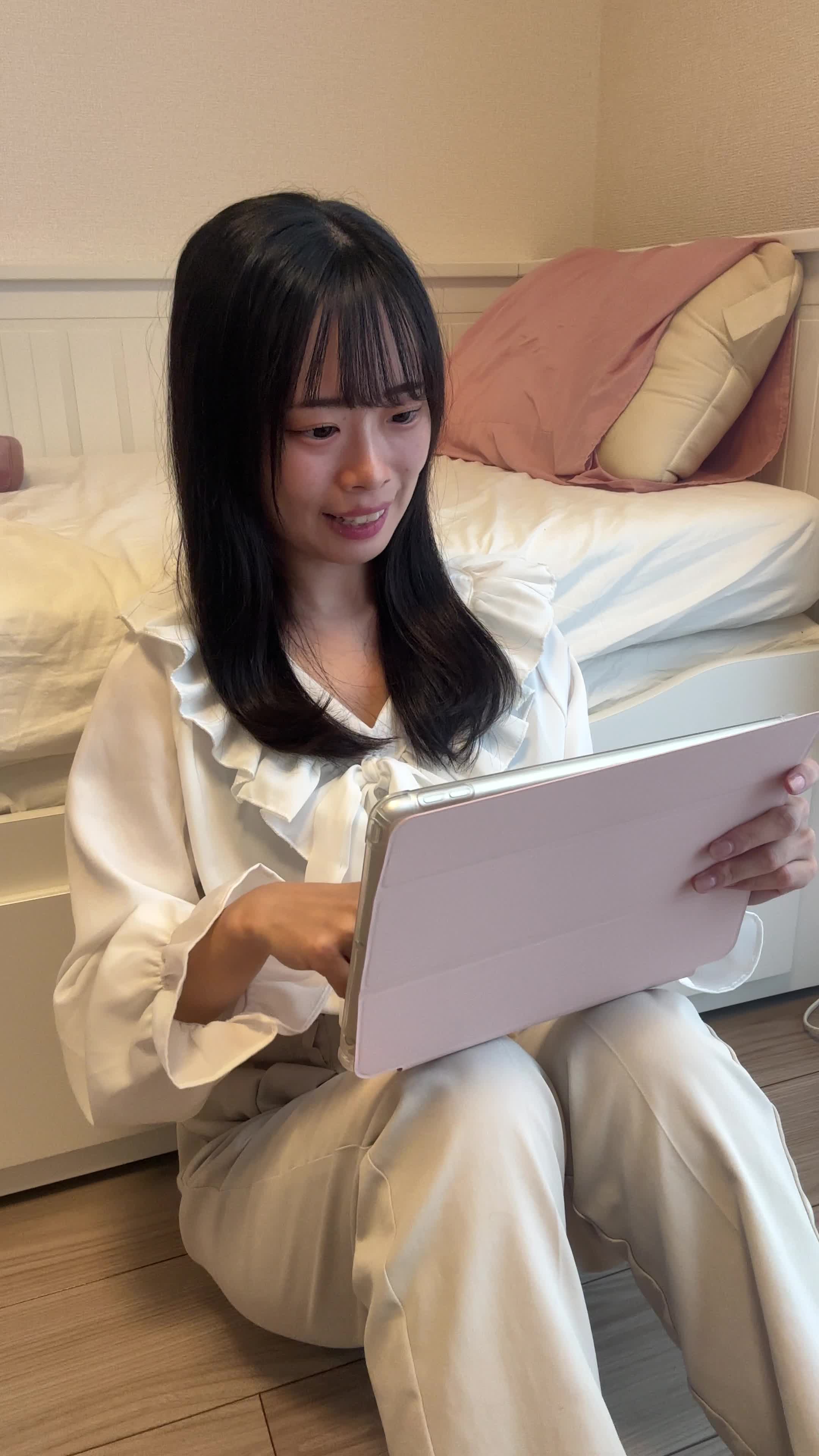 床でタブレットを操作しながら、「これ、友達にも勧めたい！」と笑顔を浮かべる様子