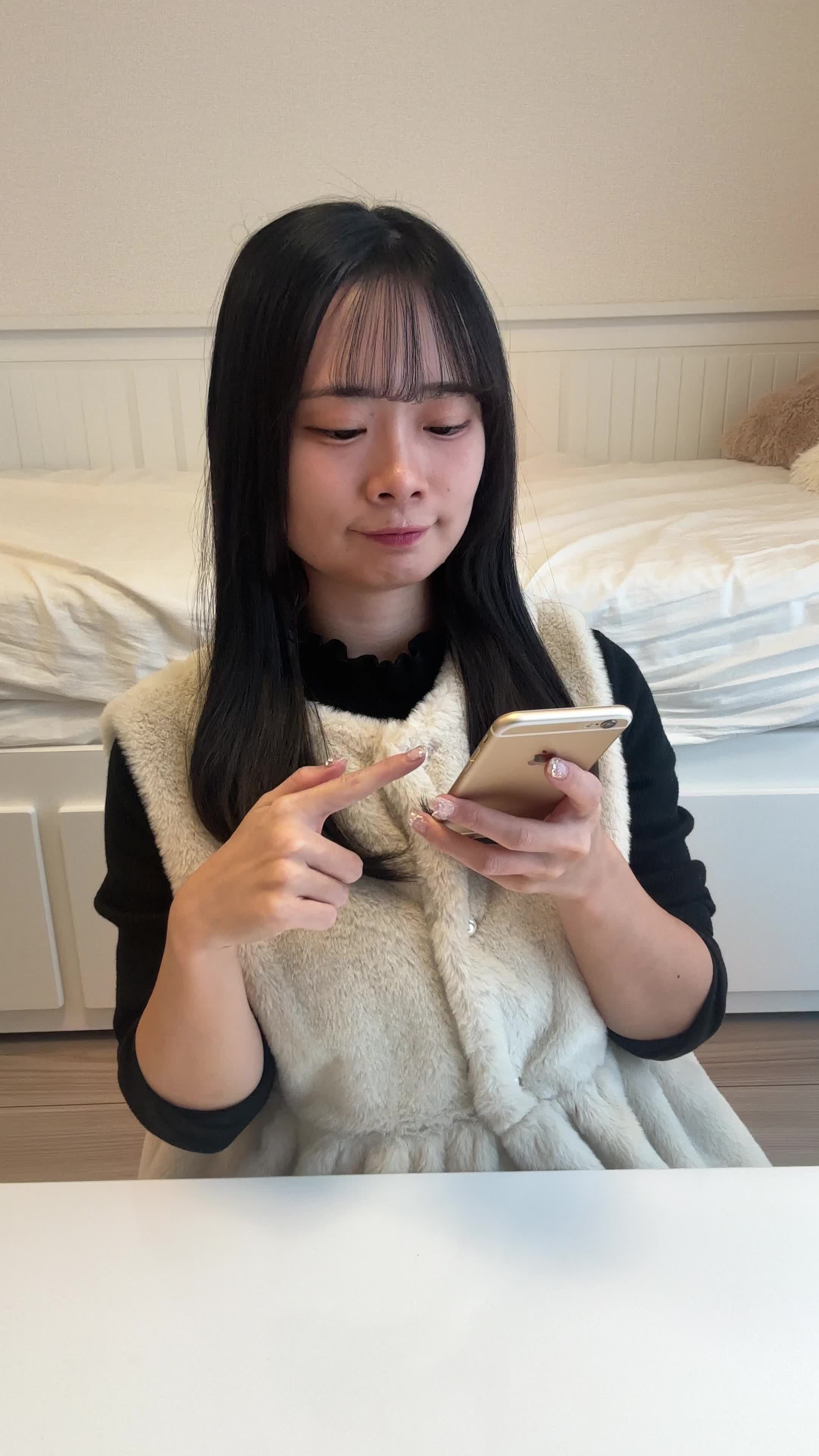 椅子に座り、スマホでカートの中身を確認しながら「これ全部買おうかな？」と悩む表情