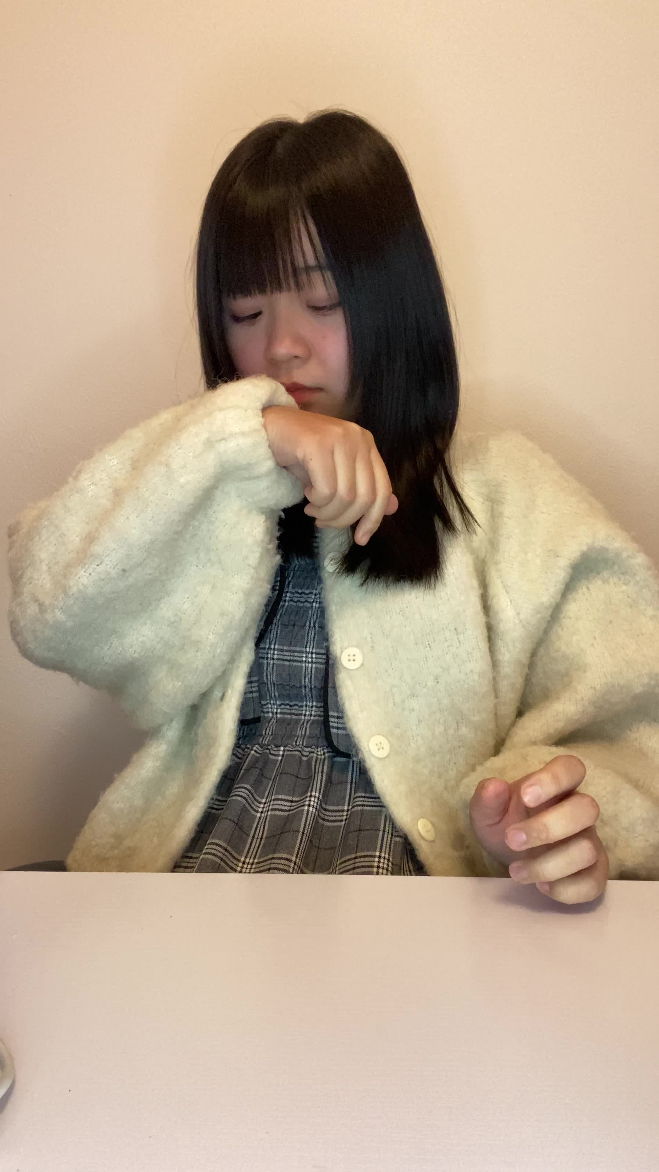 椅子に座り、少し緊張した表情で自分の服の袖を軽く嗅ぐ様子