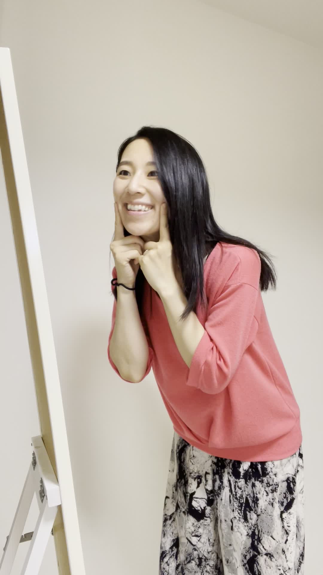 鏡越しに自分の笑顔を確認し、「今日のメイクはバッチリ」と頷く動作