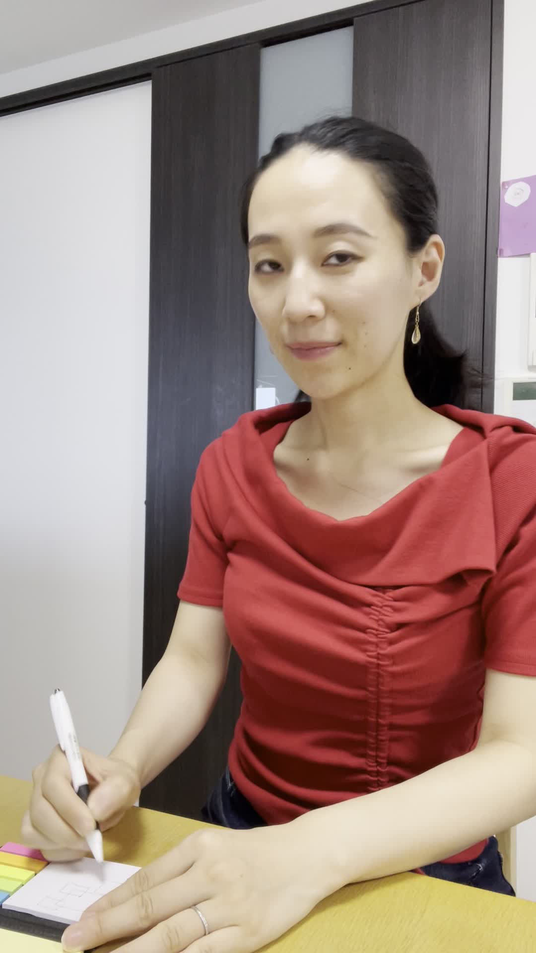 テーブルで紙に図を描いてカメラに向かって話しながら、「これが私の答えです」と説明する様子