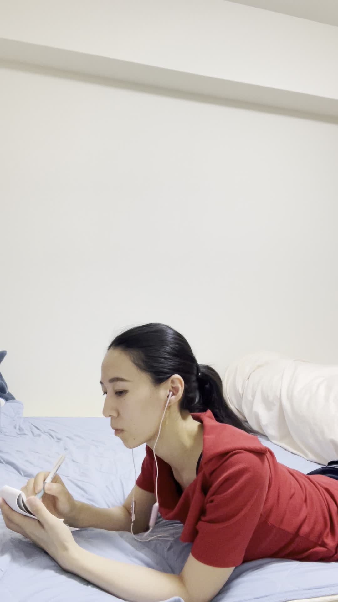 ベッドに横になり、イヤホンで音声を聞きながらメモを取ろうとする様子
