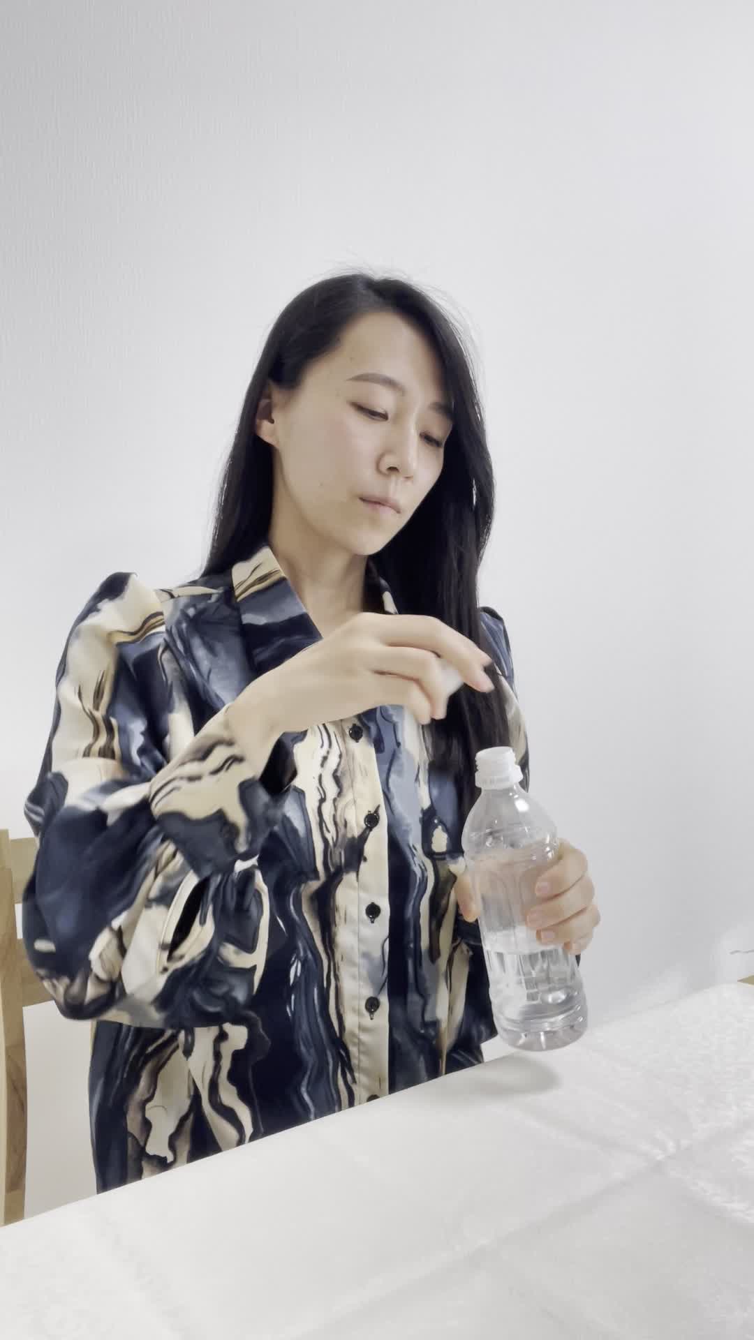 テーブルでペットボトルの蓋を開け、「もっと手軽にできる方法が欲しい」と悩む表情