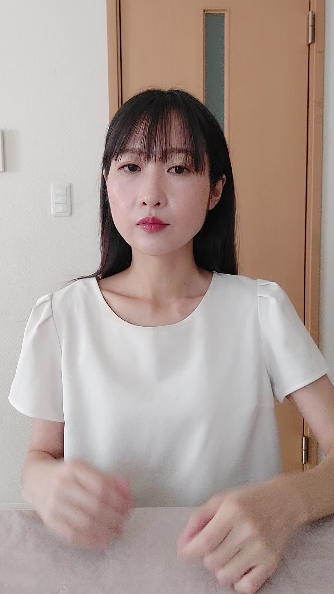 椅子に座り、少し緊張した表情で自分の服の袖を軽く嗅ぐ様子