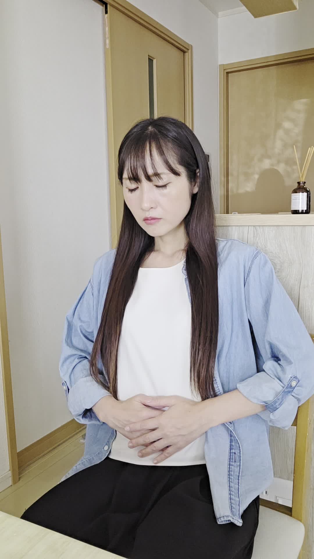 椅子に座り、お腹を軽く押さえながら「ずっと痛みが続いている…」と苦しそうな表情