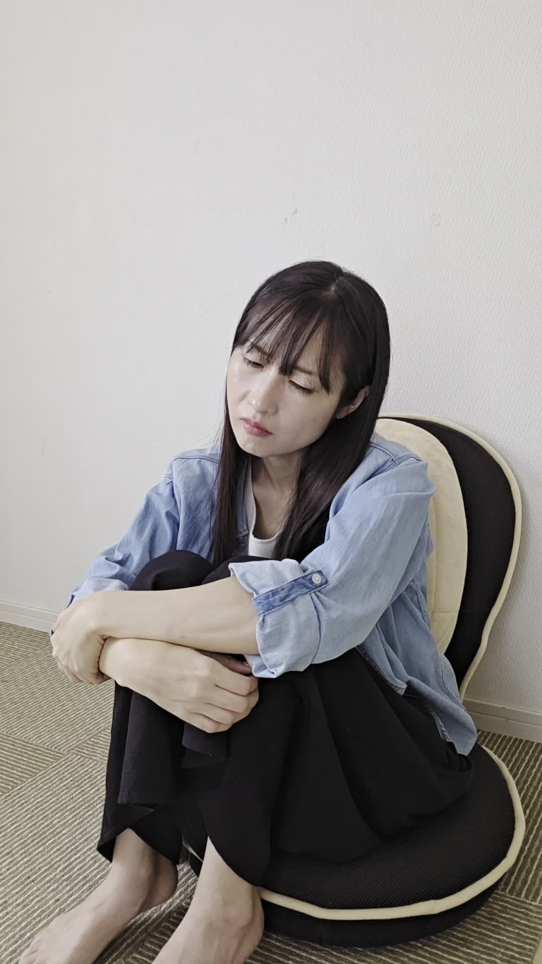 椅子で膝を抱え、「体がだるくて動けない」と頭を抱える様子