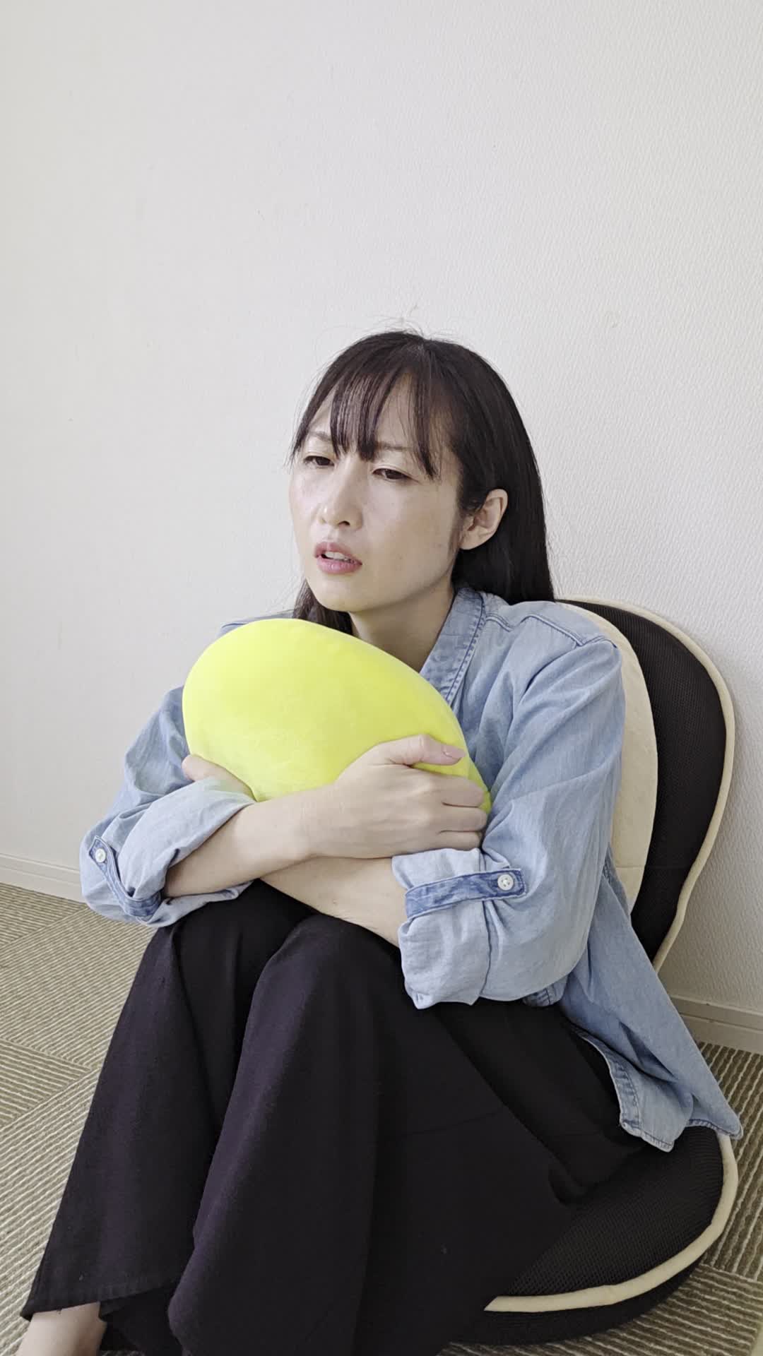 椅子でクッションを抱え、「腸が動いていない感じがして不安そうに考える」表情