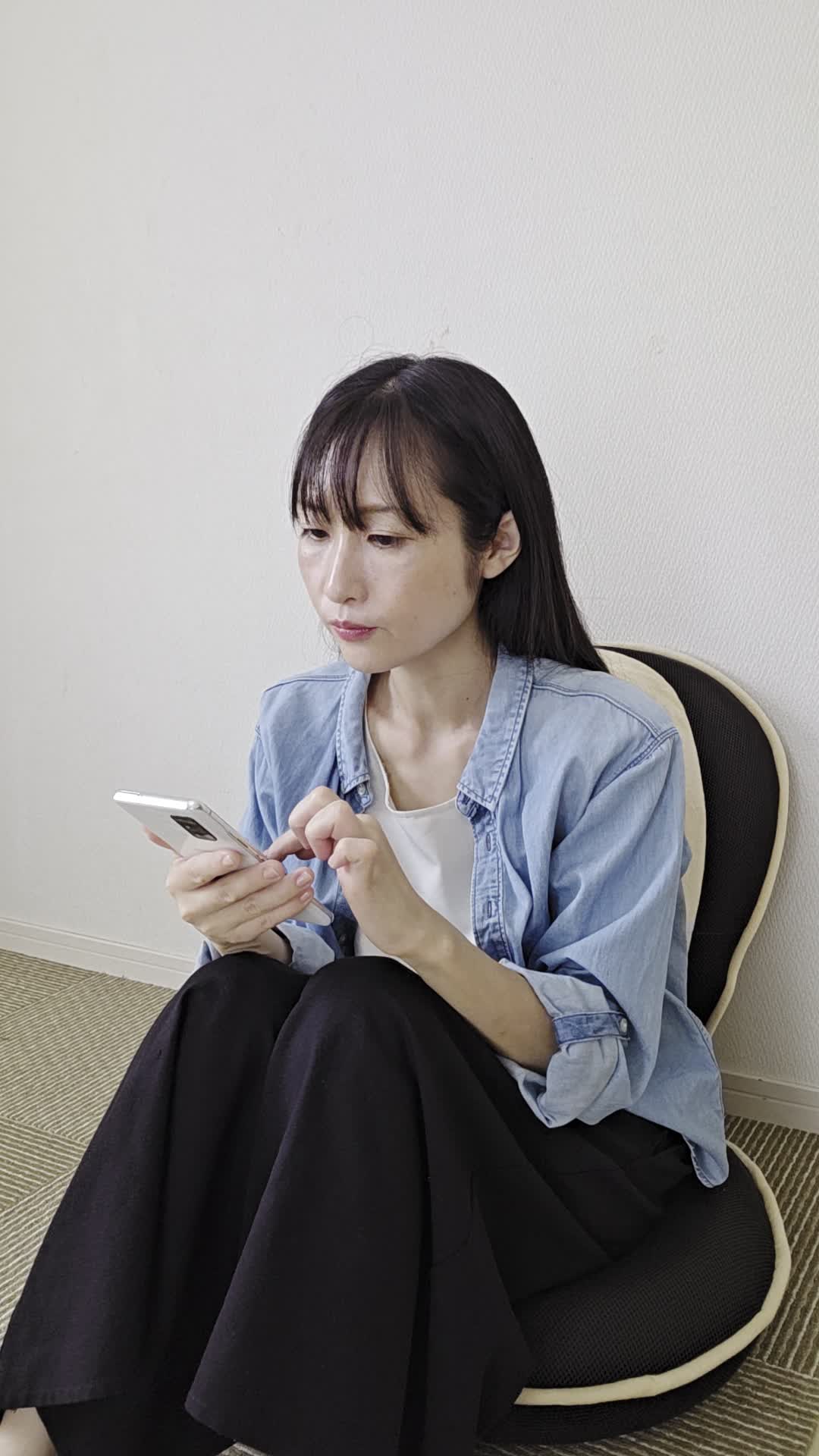 椅子でスマホを見ながら、「腸活の方法を見つけて試したいけど迷う」表情