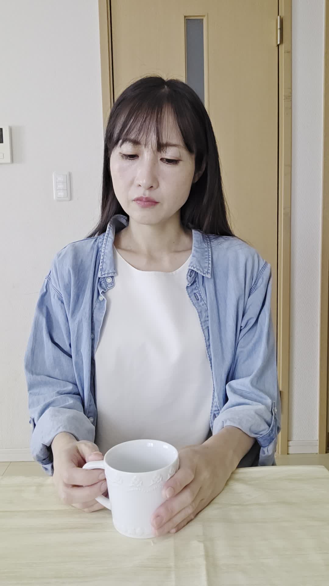 テーブルでカップを手に取り、「腸の不調がこんなに続くとは…」と困った顔をする様子