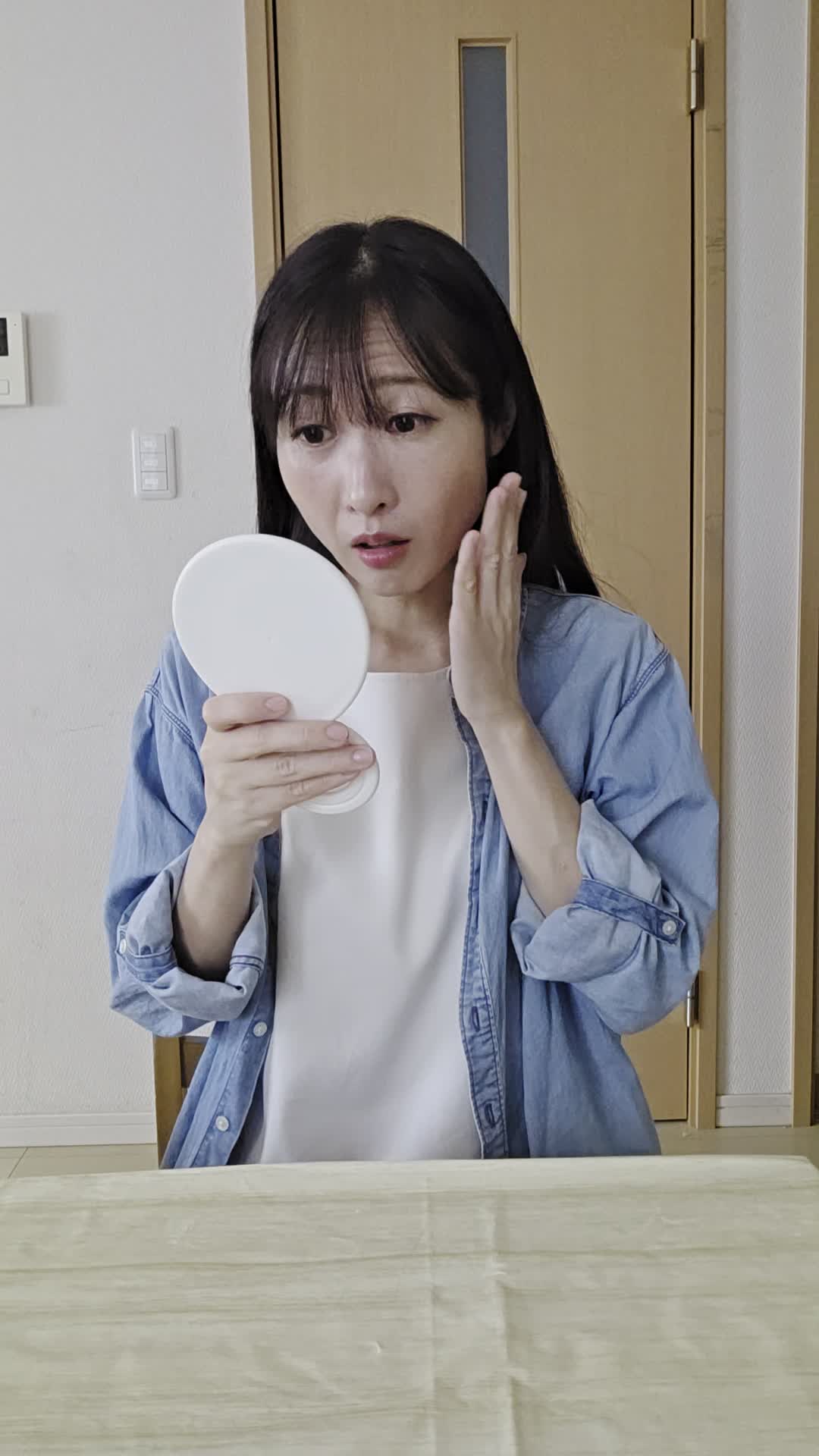 テーブルで鏡を見ながら、「顔色が悪くて腸の不調のせいかも」と気にする様子