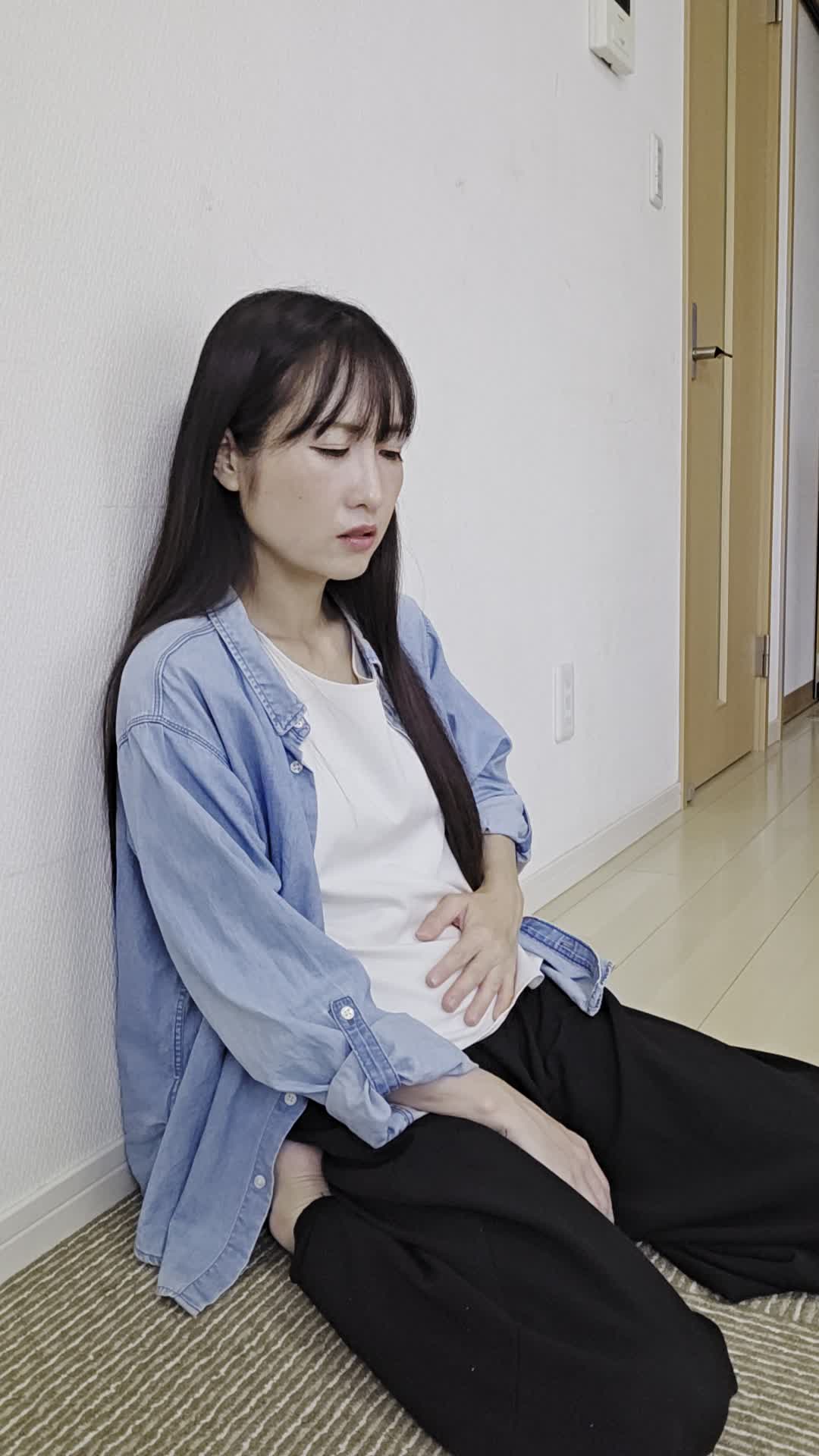床で膝を崩して座り、「お腹の痛みで集中できない」と悩む真剣な表情