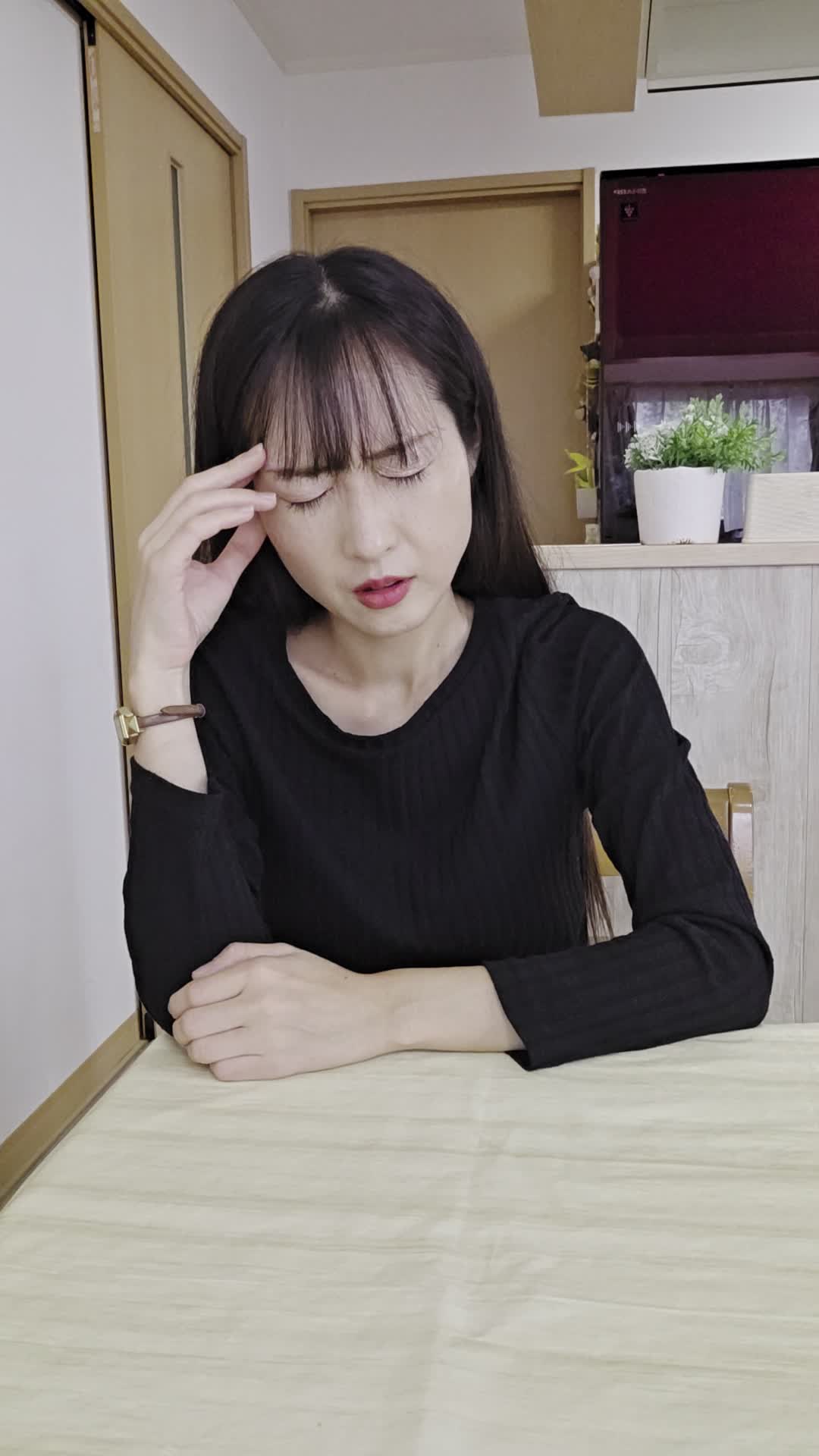椅子に座り、手でこめかみを押さえながら「最近ずっと頭が重い」と困った表情