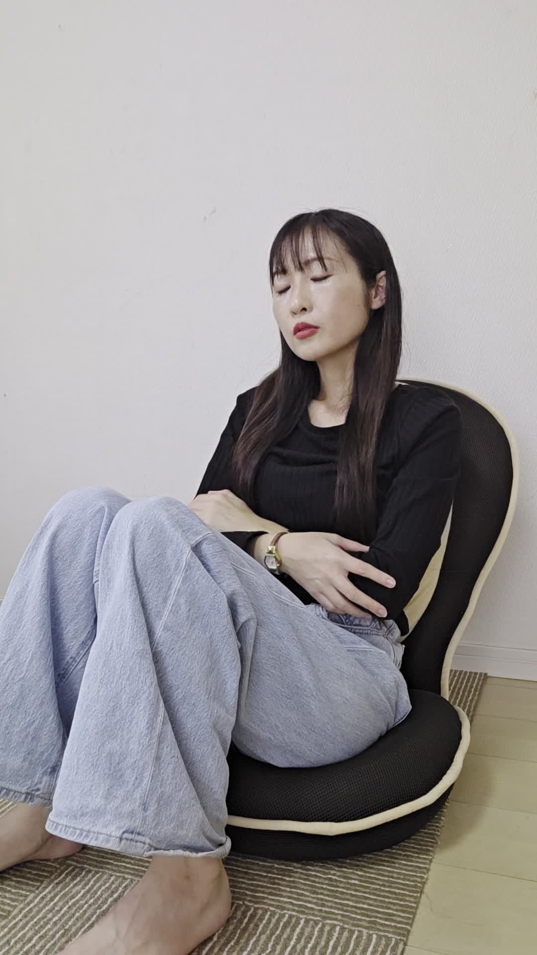 ソファで膝を曲げながら、「疲れた体に何が必要か考えて健康ドリンクを検討する」様子