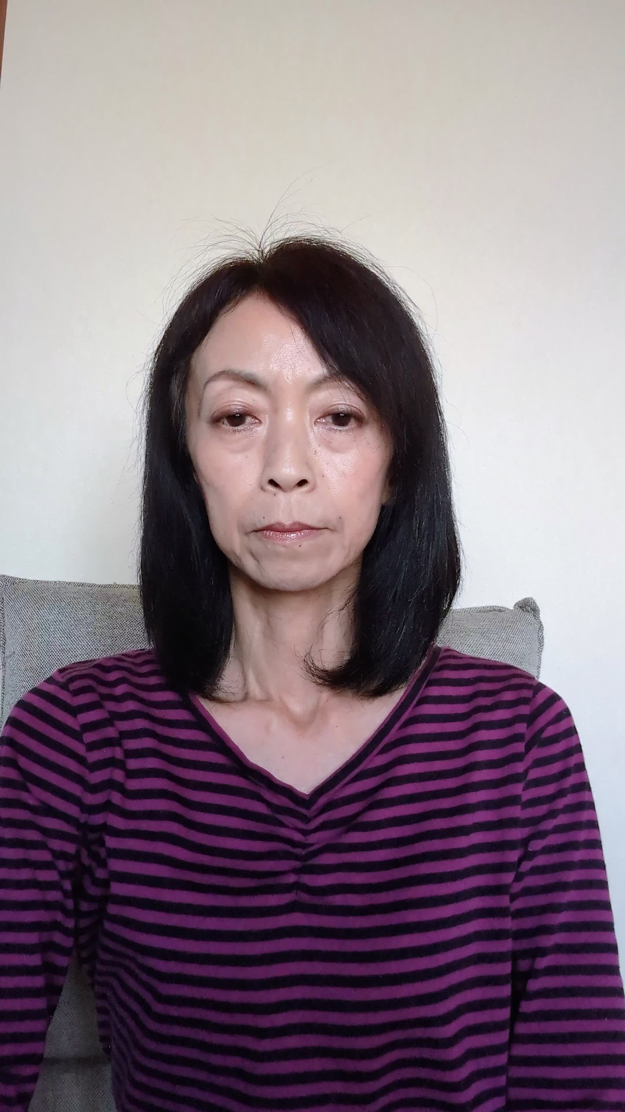 椅子に座り、少し緊張した表情で自分の服の袖を軽く嗅ぐ様子