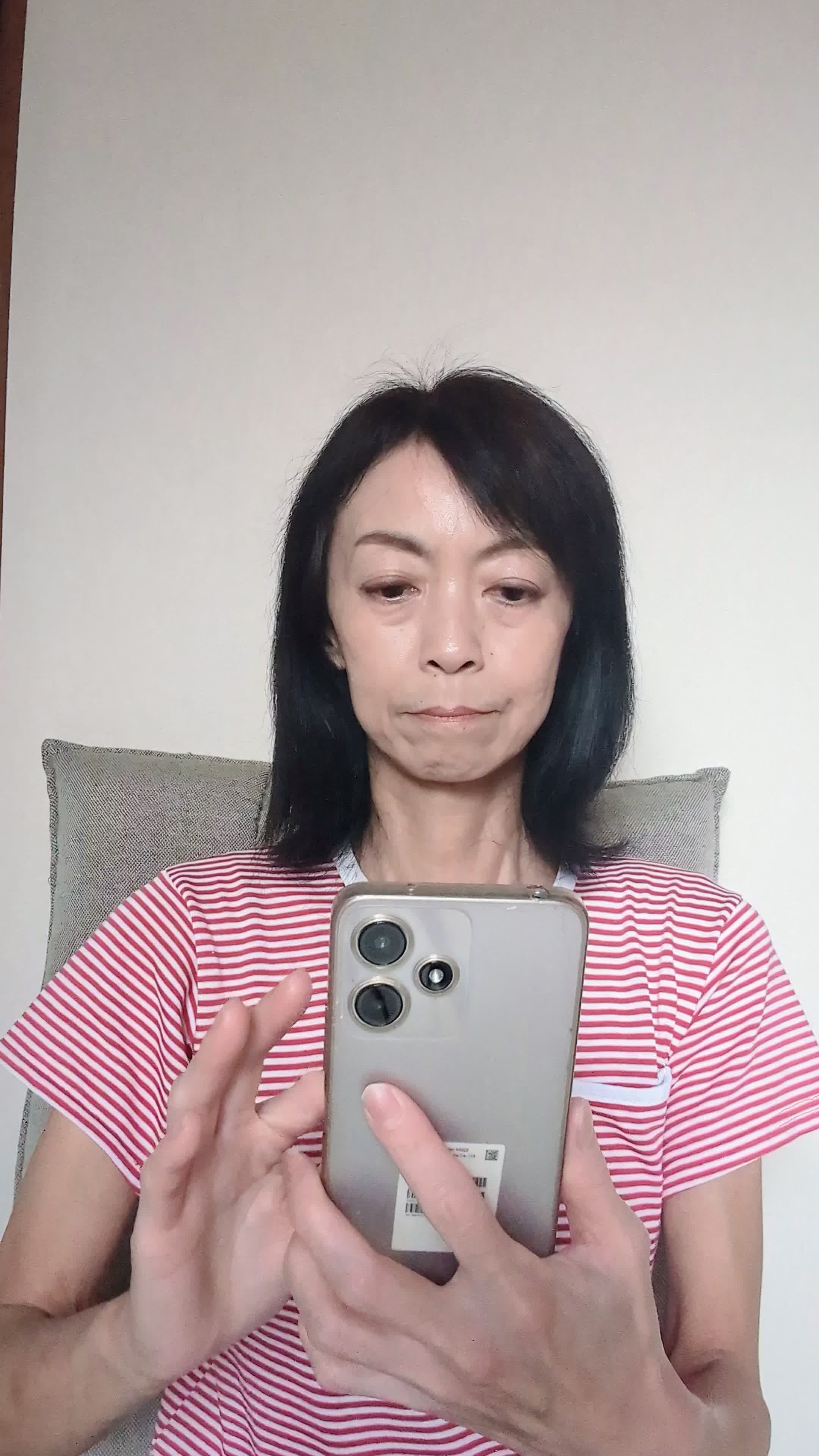 椅子に腰掛け、スマホの画面を見て「白髪ケアの口コミを読んで納得する」表情