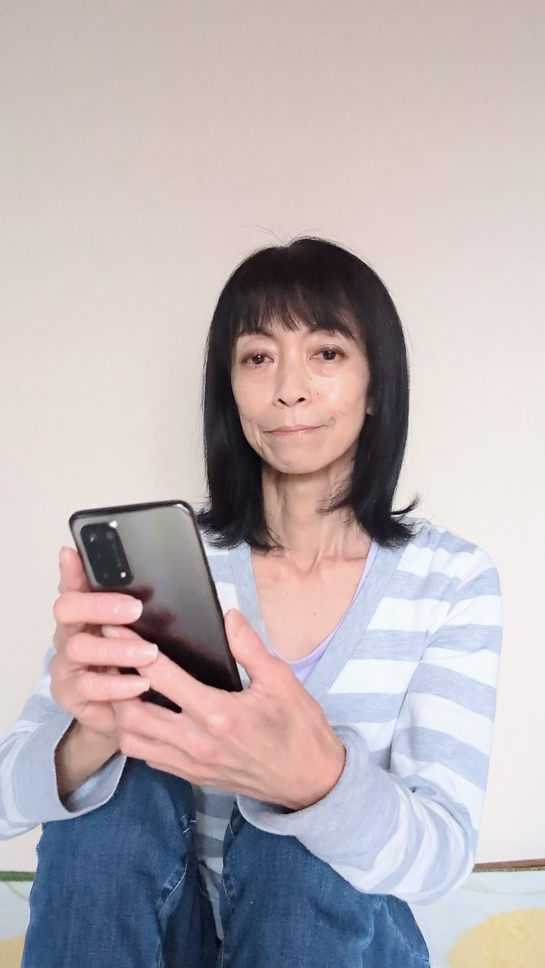 床に座り込み、「これなら挑戦できるかも」とスマホの画面を見て微笑む姿