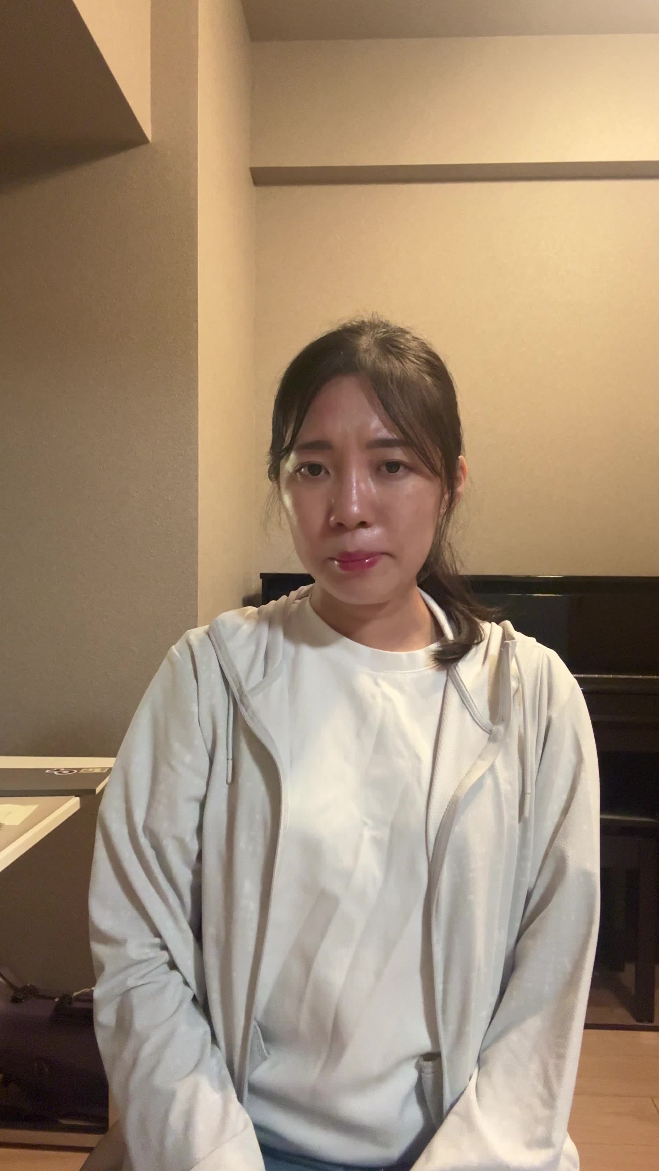 椅子に座り、少し緊張した表情で自分の服の袖を軽く嗅ぐ様子