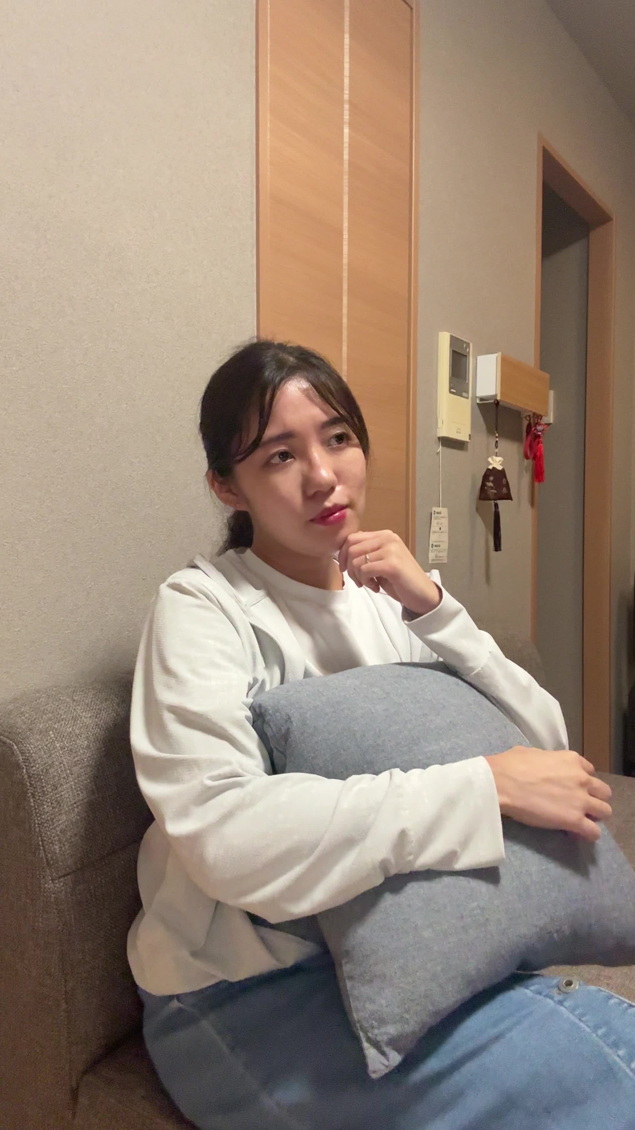 ソファでクッションを抱え、「これで匂いが改善するかな？」と悩む真剣な表情