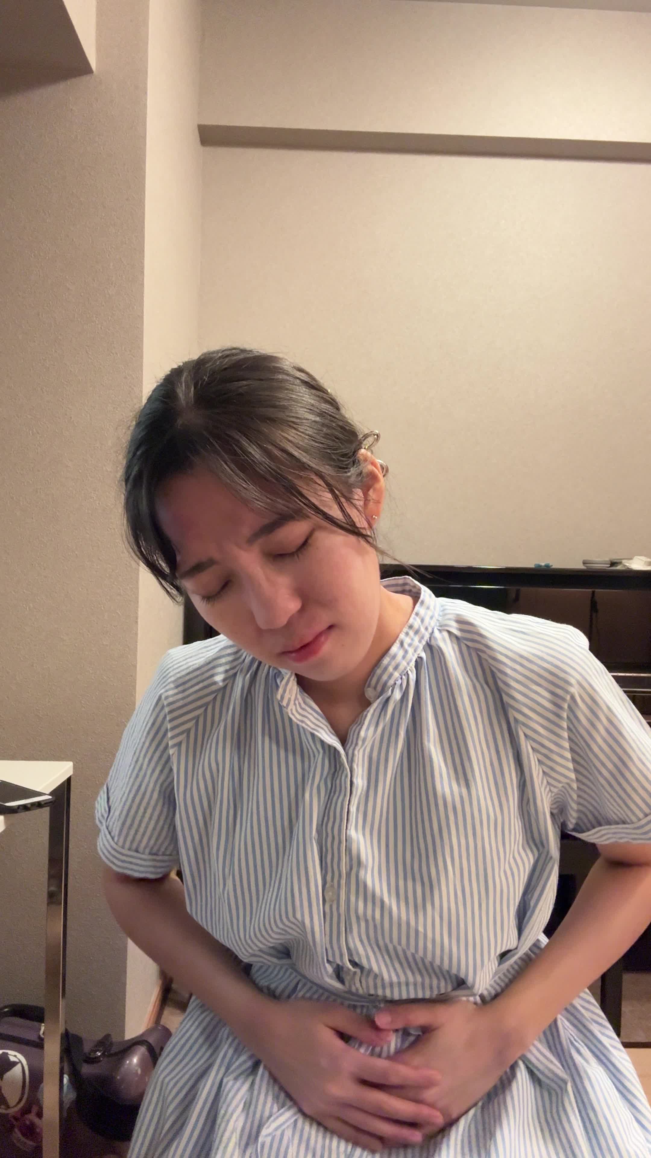 椅子に座り、お腹を軽く押さえながら「ずっと痛みが続いている…」と苦しそうな表情