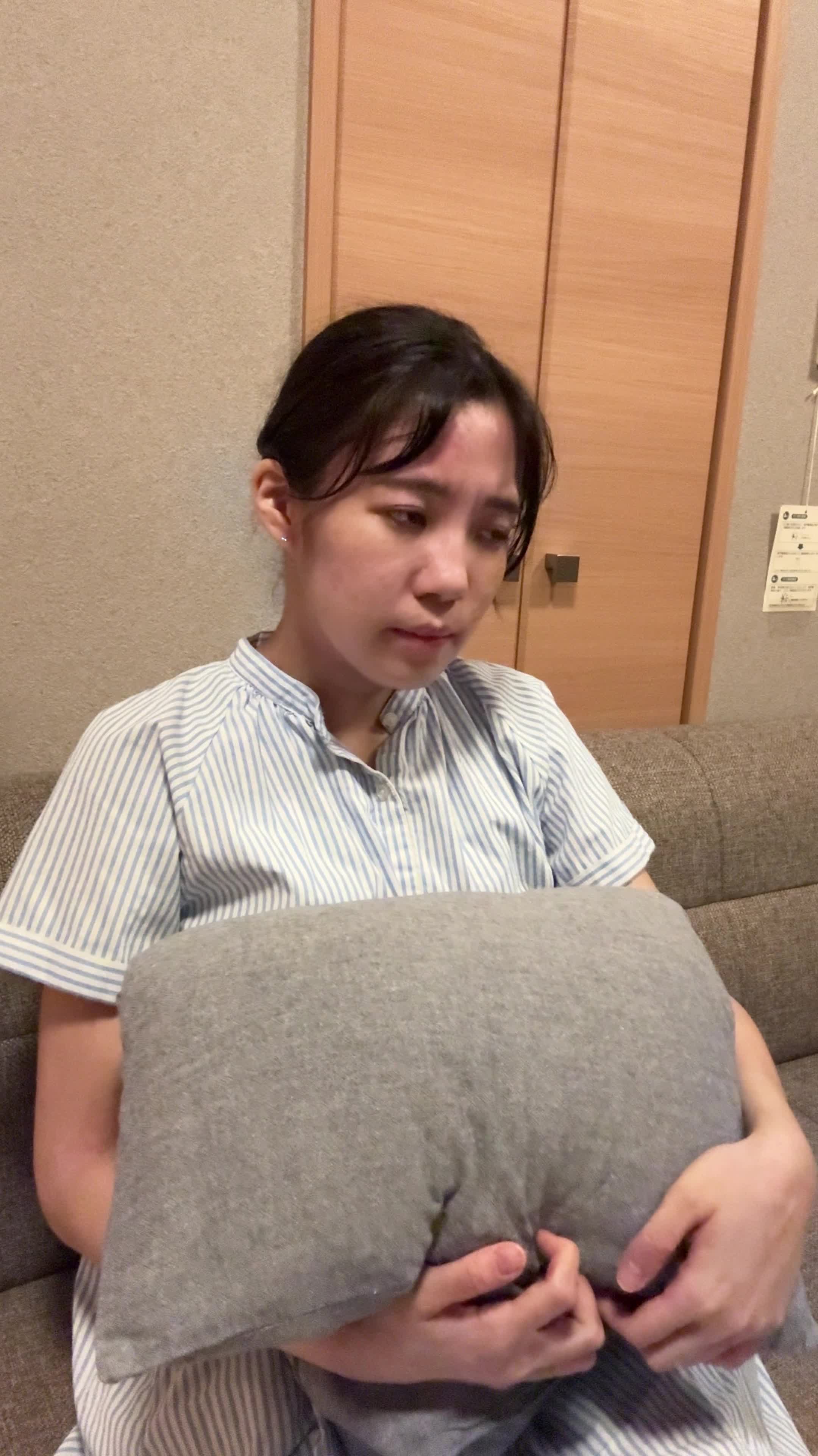 ソファでクッションを抱え、「腸が動いていない感じがして不安そうに考える」表情