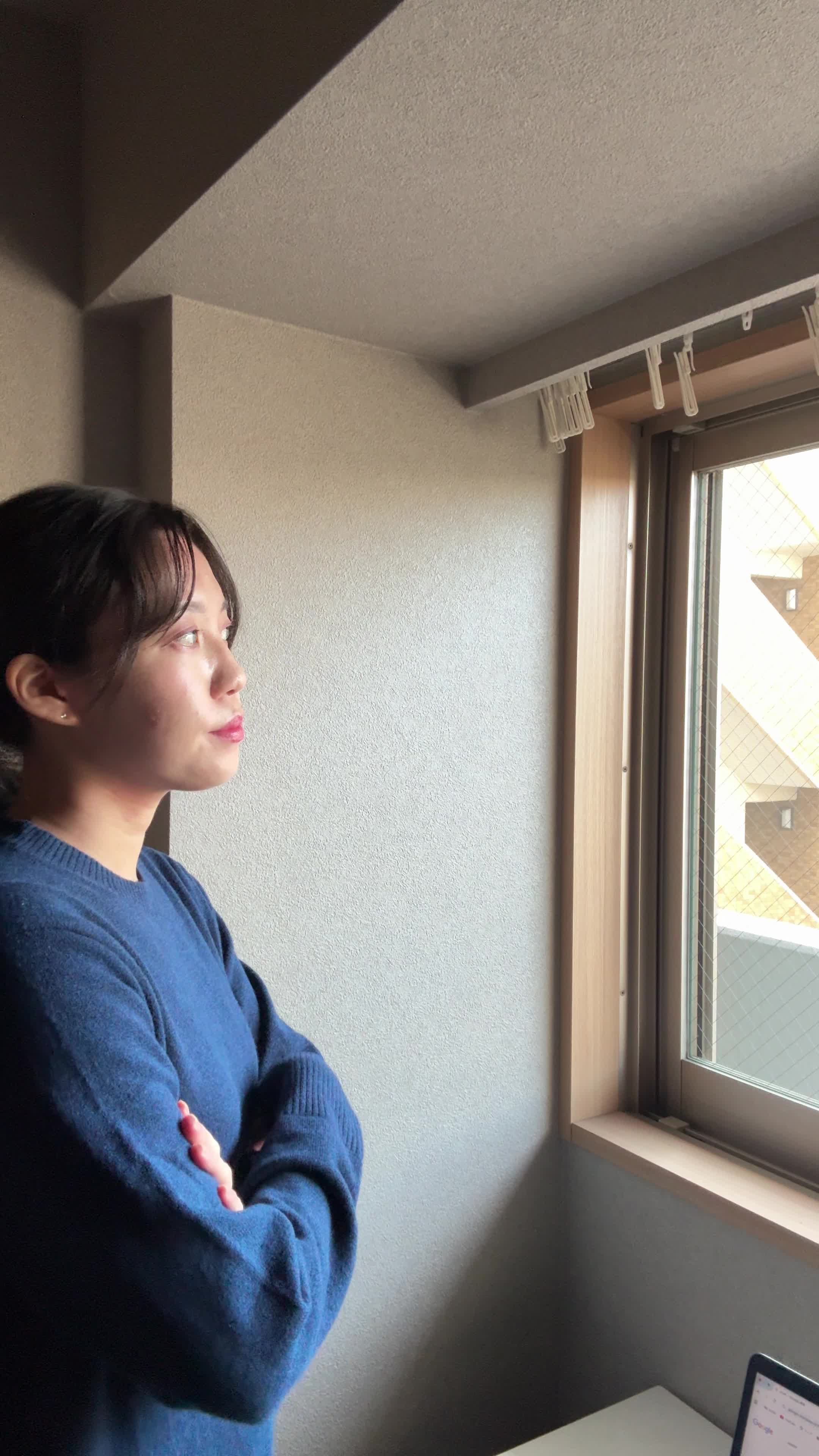 窓の方に歩いて行き、外を眺めながら軽く首を傾げる