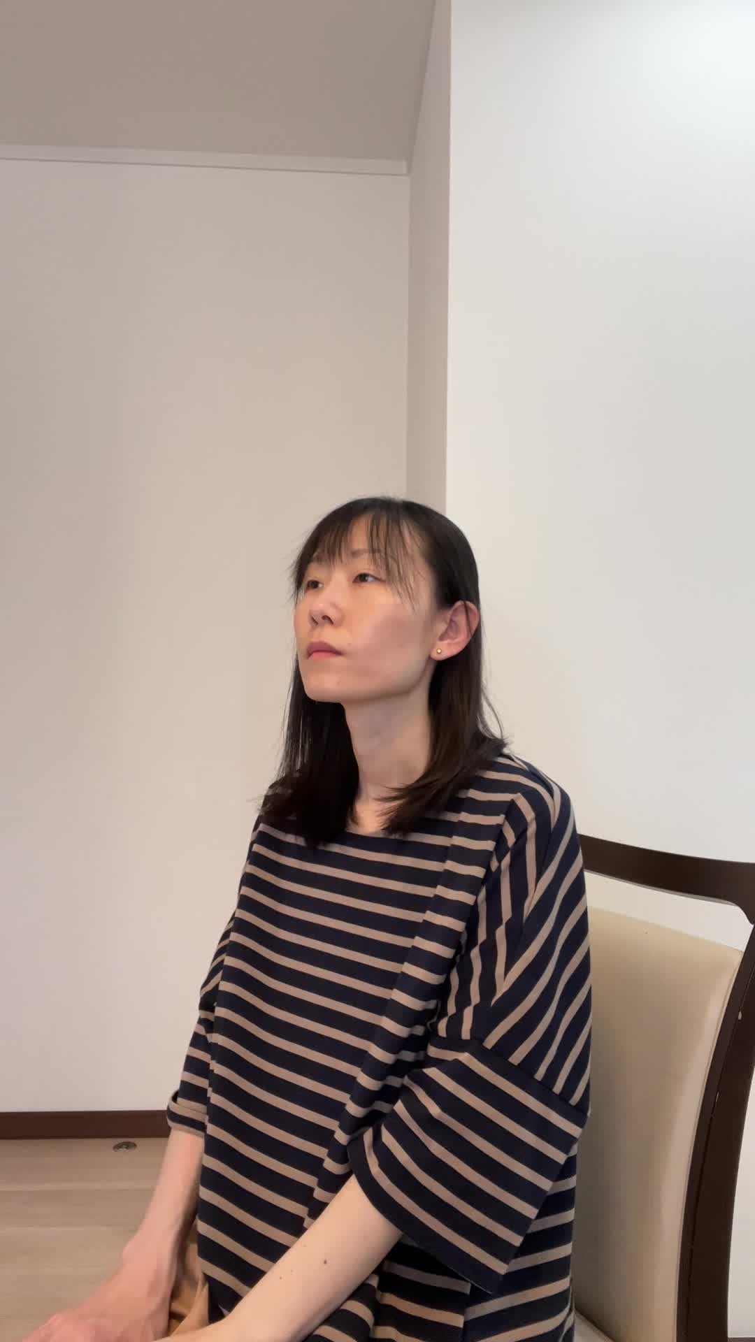 椅子から立ち上がり、「仕事中に疲れが出やすいのがつらい」と肩を回す動作