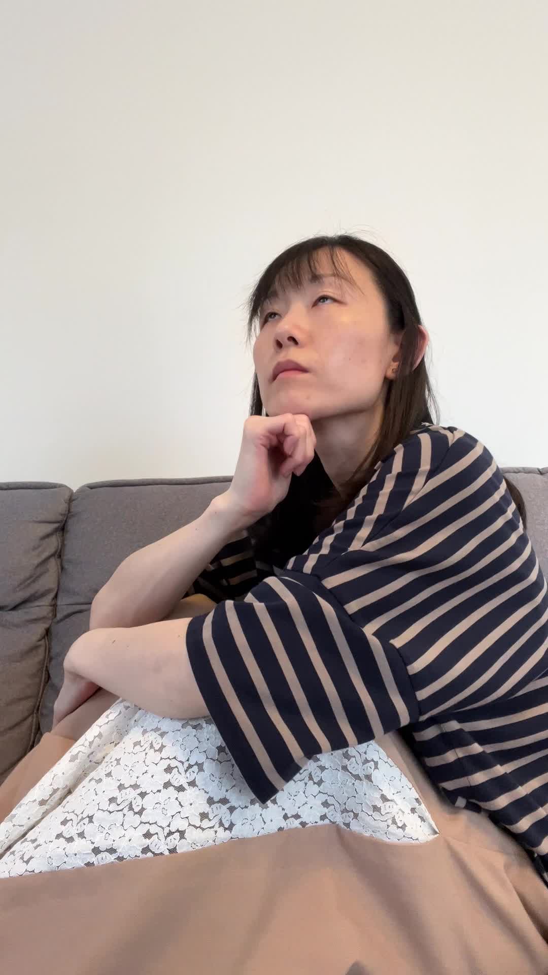 ソファで膝を曲げながら、「疲れた体に何が必要か考えて健康ドリンクを検討する」様子
