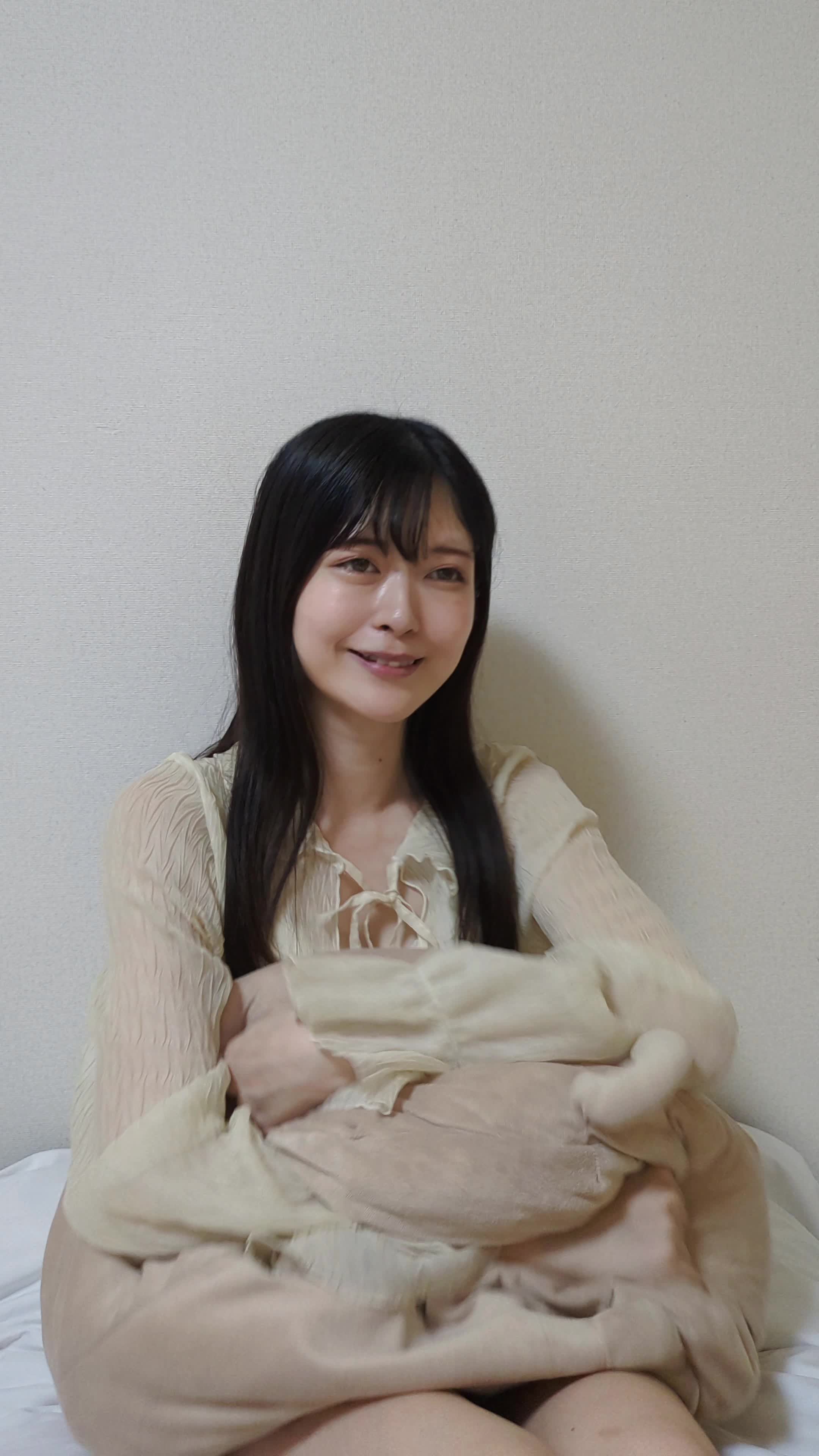 ソファでクッションを抱き、「やっぱり笑顔が大事だよね」と頷く動作