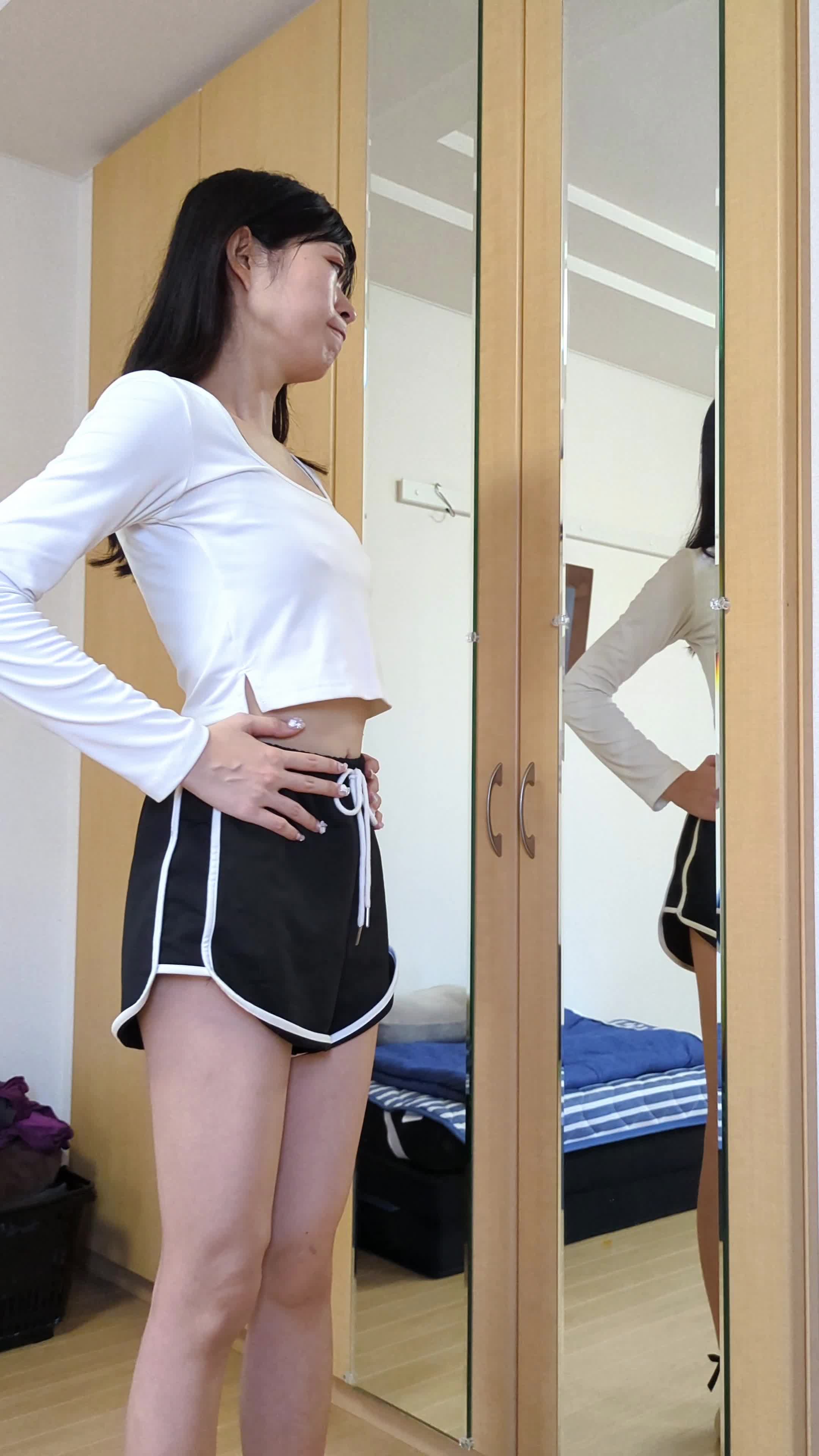 鏡の前でウエストを手で軽く触りながら考え込む表情をしている