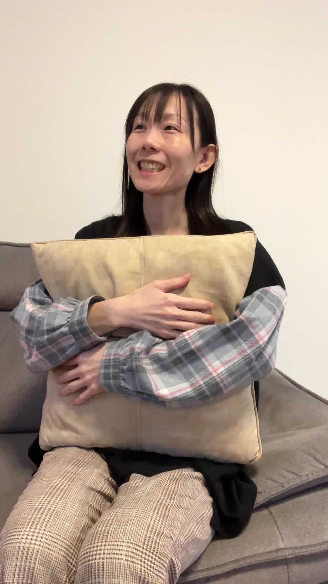 ソファでクッションを抱き、「やっぱり笑顔が大事だよね」と頷く動作