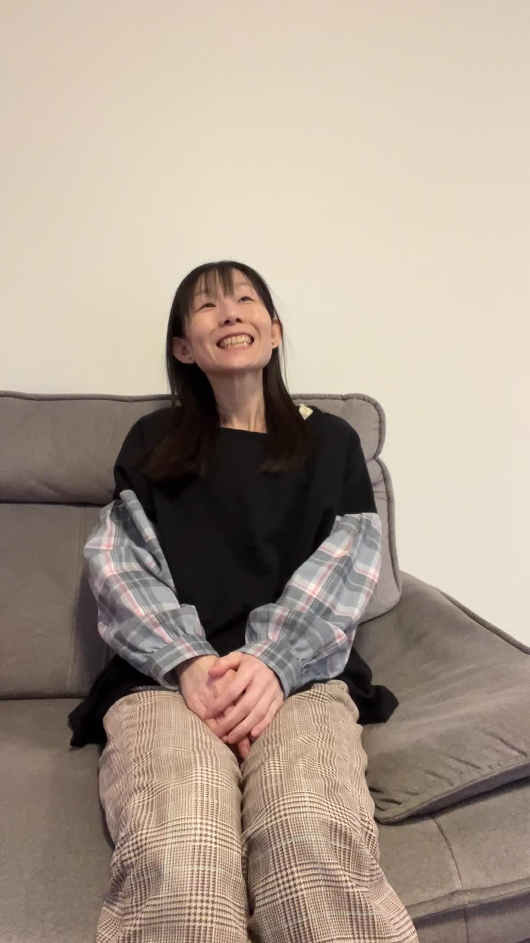 ソファに深く座り、笑顔の練習をしながら「まだまだ…」と首を傾ける仕草