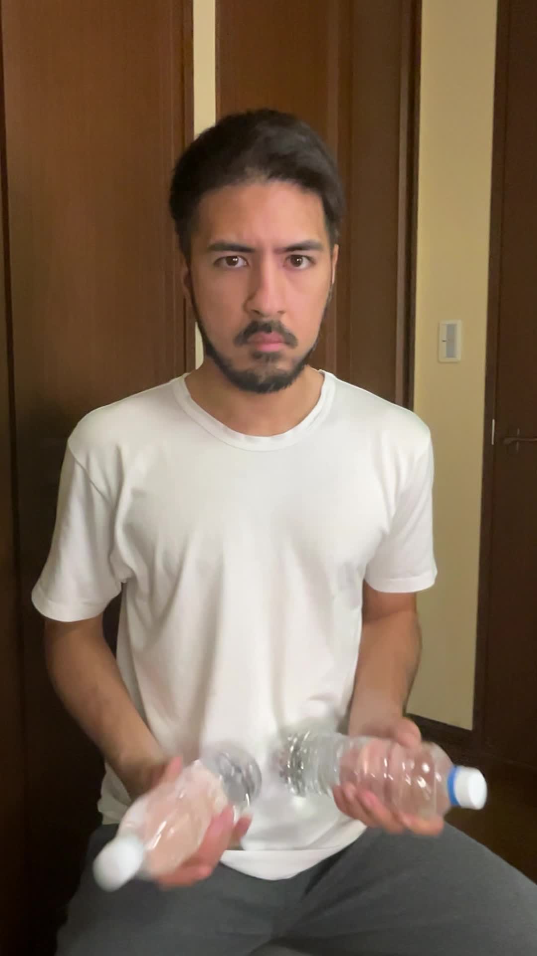 椅子に座り、ペットボトルをダンベル代わりにして軽く腕を曲げる仕草